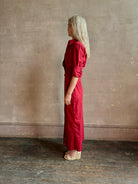 Mature woman wearing New Earl wrap shirt Dress from TWP rendered in a vibrant red and crafted from cotton poplin in the USA with 1/2 sleeves, collar, asymetrical button top and maxi length dress