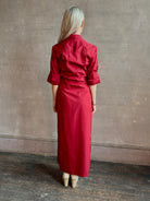 Mature woman wearing New Earl wrap shirt Dress from TWP rendered in a vibrant red and crafted from cotton poplin in the USA with 1/2 sleeves, collar, asymetrical button top and maxi length dress