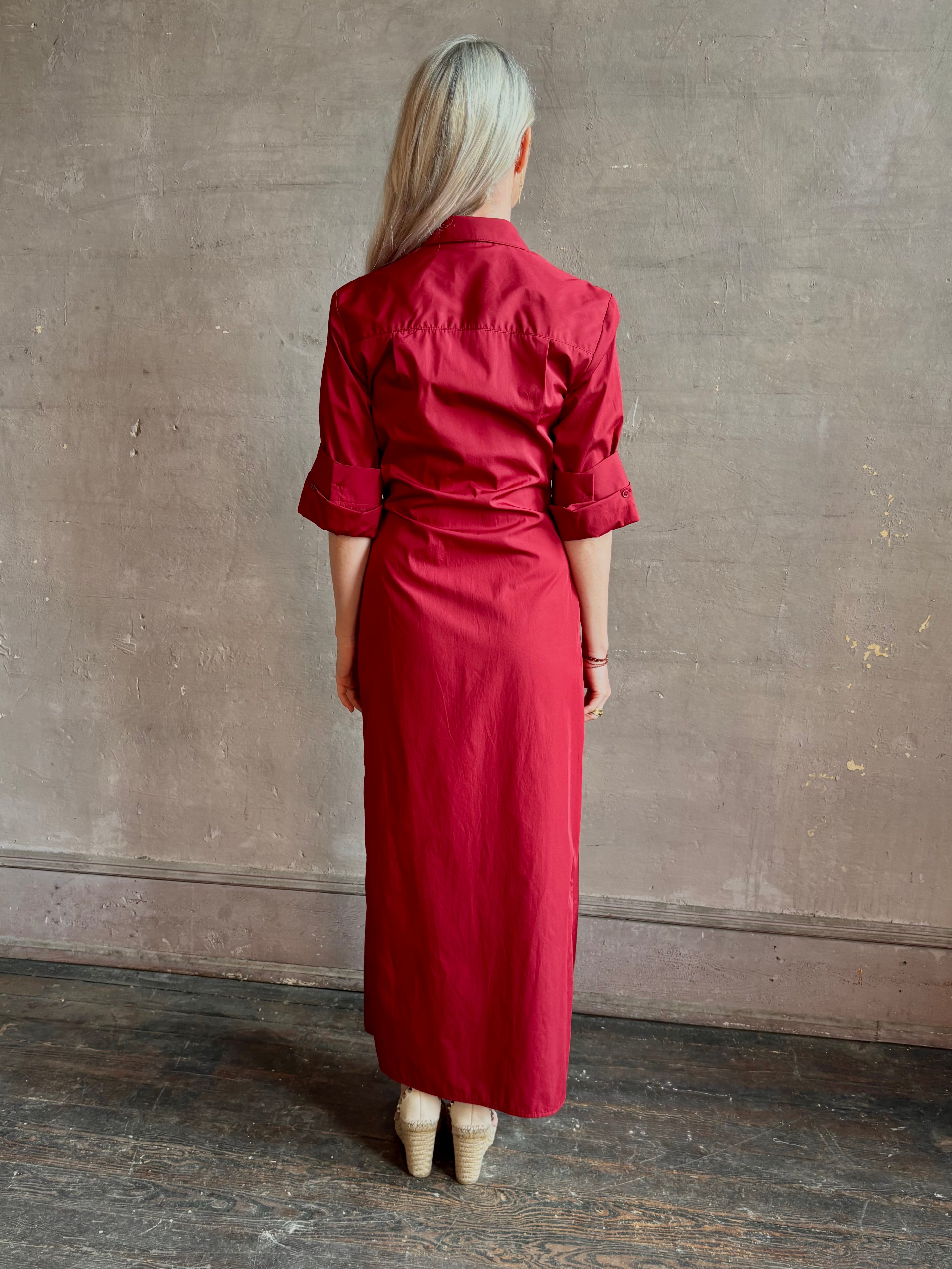 Mature woman wearing New Earl wrap shirt Dress from TWP rendered in a vibrant red and crafted from cotton poplin in the USA with 1/2 sleeves, collar, asymetrical button top and maxi length dress