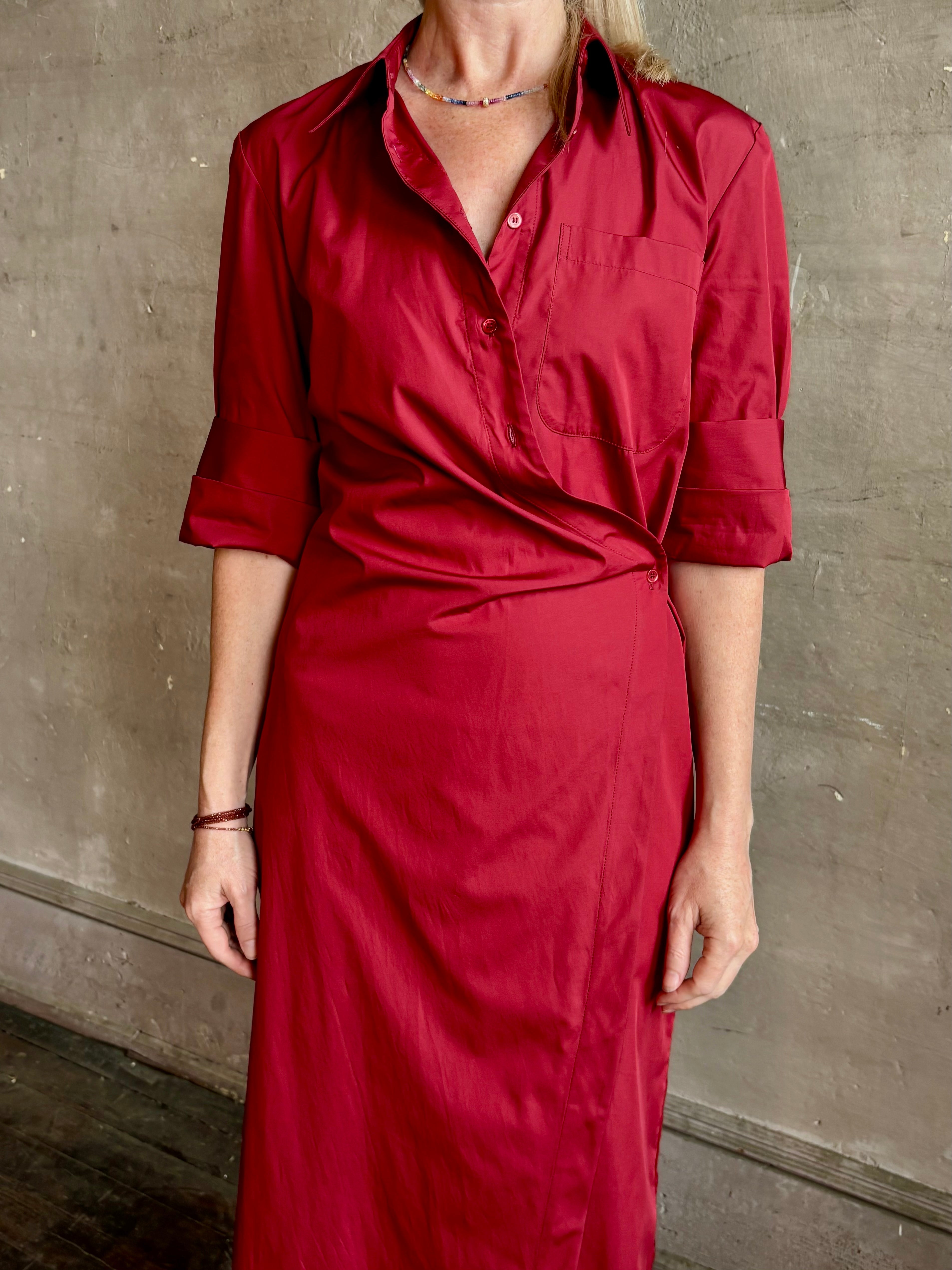 Mature woman wearing New Earl wrap shirt Dress from TWP rendered in a vibrant red and crafted from cotton poplin in the USA with 1/2 sleeves, collar, asymetrical button top and maxi length dress