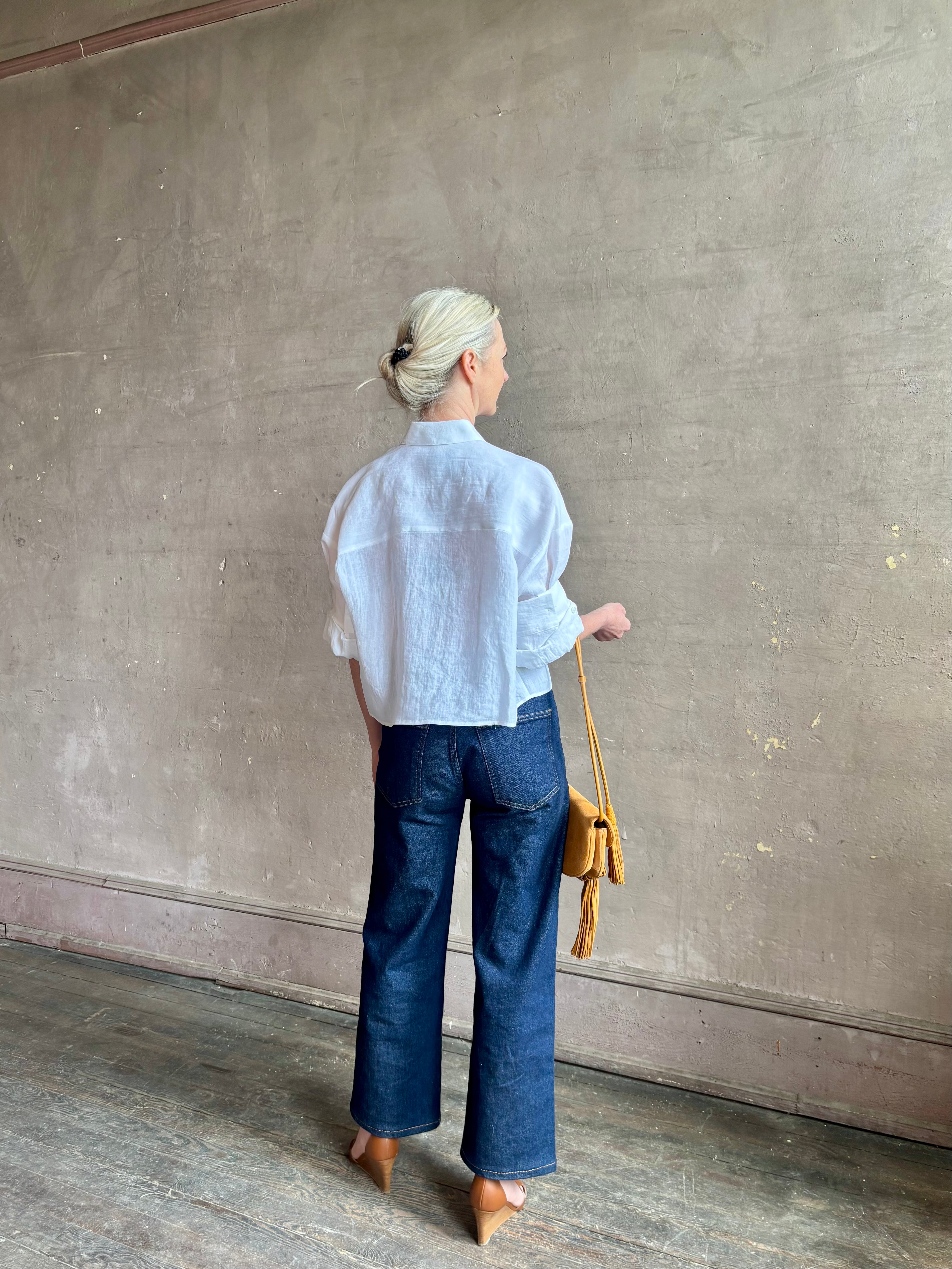 Mature woman wearing the Next Ex Top from TWP rendered in a crisp white and crafted from premium linen in New York City, this luxury linen top offers effortless cool girl with an intentionally oversized boxy silhouette with tailored half sleeve cuffs, collared button - down menswear inspired with a single front pocket