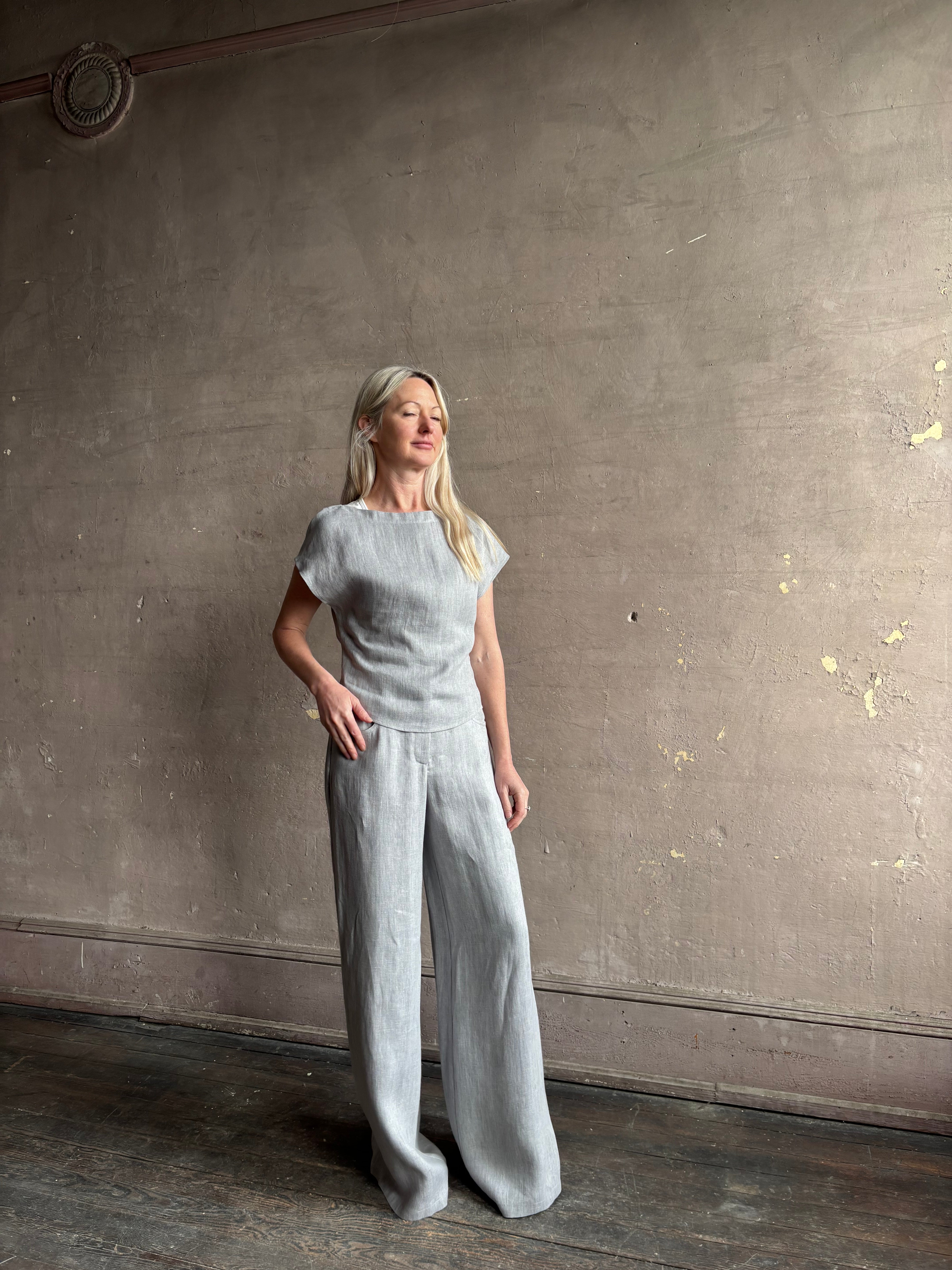 Mature woman wearing the Simple T Top from TWP that is rendered in a light heather grey hemp with short sleeves and boat neckline
