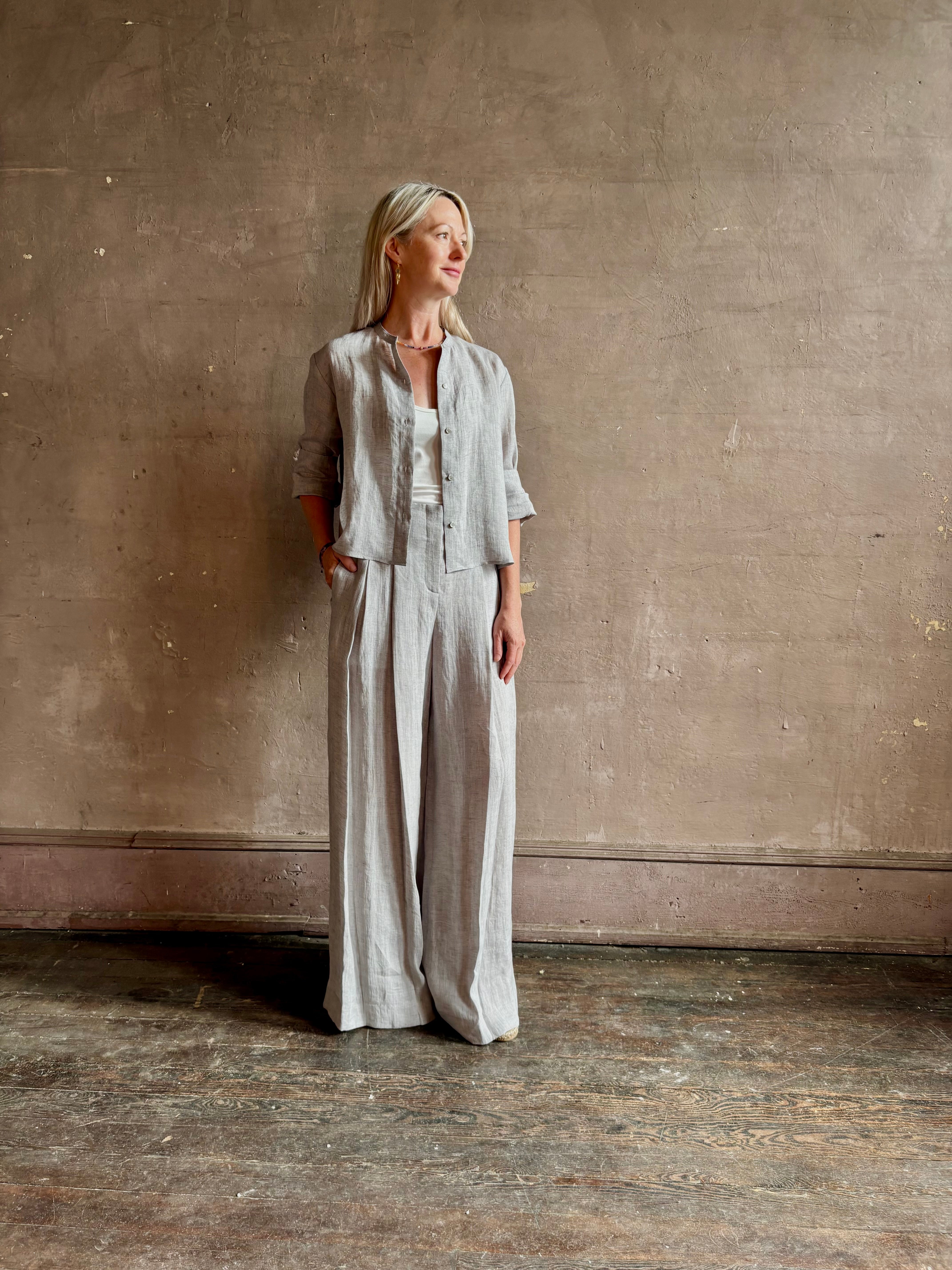 Mature woman wearing Stand Collar Cut Off Top from TWP rendered in a versatile light heather grey and crafted from 100% hemp with round mandarin collar, button front, half sleeves and made in the USA