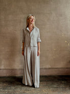 Mature woman wearing Stand Collar Cut Off Top from TWP rendered in a versatile light heather grey and crafted from 100% hemp with round mandarin collar, button front, half sleeves and made in the USA