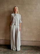 Mature woman wearing Stand Collar Cut Off Top from TWP rendered in a versatile light heather grey and crafted from 100% hemp with round mandarin collar, button front, half sleeves and made in the USA