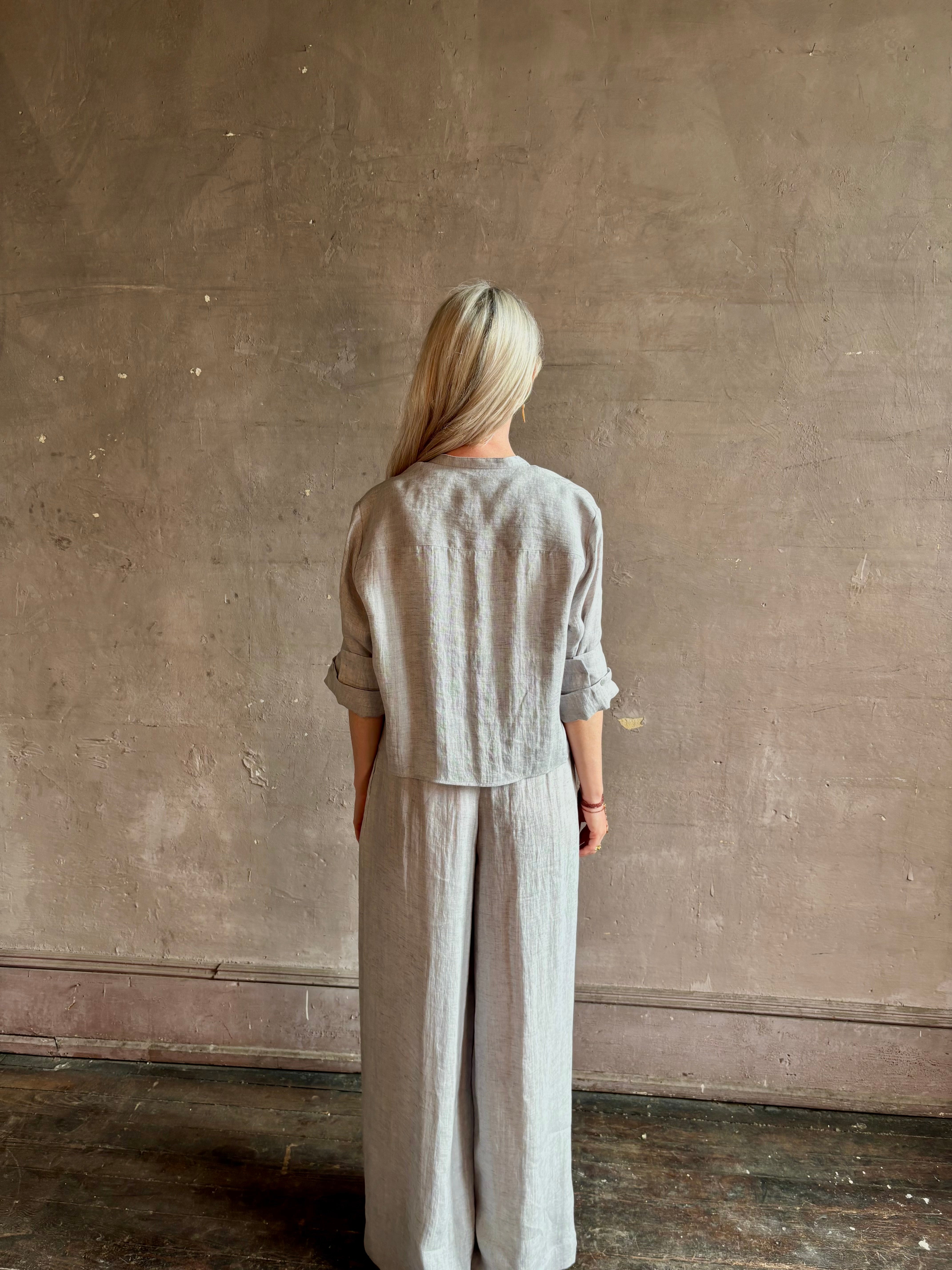 Mature woman wearing Stand Collar Cut Off Top from TWP rendered in a versatile light heather grey and crafted from 100% hemp with round mandarin collar, button front, half sleeves and made in the USA