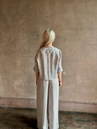 Mature woman wearing Stand Collar Cut Off Top from TWP rendered in a versatile light heather grey and crafted from 100% hemp with round mandarin collar, button front, half sleeves and made in the USA