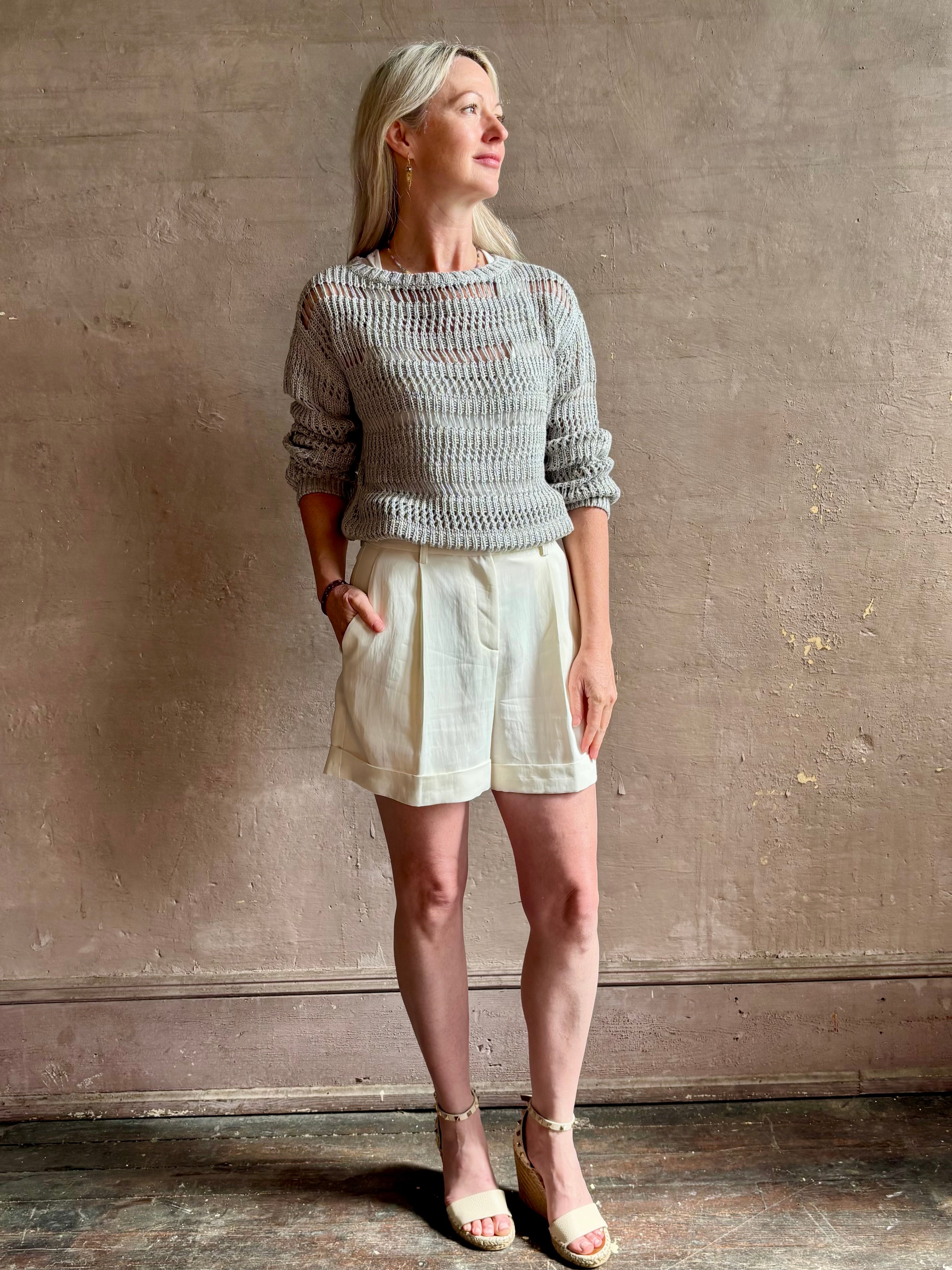 Mature woman wearing Wide Neck Long Sleeve  open knit Sweater from TWP in a luxuriously wearable everyday essential rendered in a soft light grey and crafted from an elevated blend of European flax linen and recycled mulberry silk