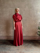 Mature woman wearing Wish You Would blouse from TWP rendered in a rich currant red and crafted from a luxurious silk blend with a mock neck,  asymetrical design and draping short sleeves shoulder button closure and matching skirt