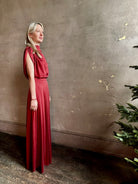 Mature woman wearing Wish You Would blouse from TWP rendered in a rich currant red and crafted from a luxurious silk blend with a mock neck,  asymetrical design and draping short sleeves shoulder button closure and matching skirt