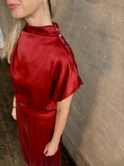 Mature woman wearing Wish You Would blouse from TWP rendered in a rich currant red and crafted from a luxurious silk blend with a mock neck,  asymetrical design and draping short sleeves shoulder button closure