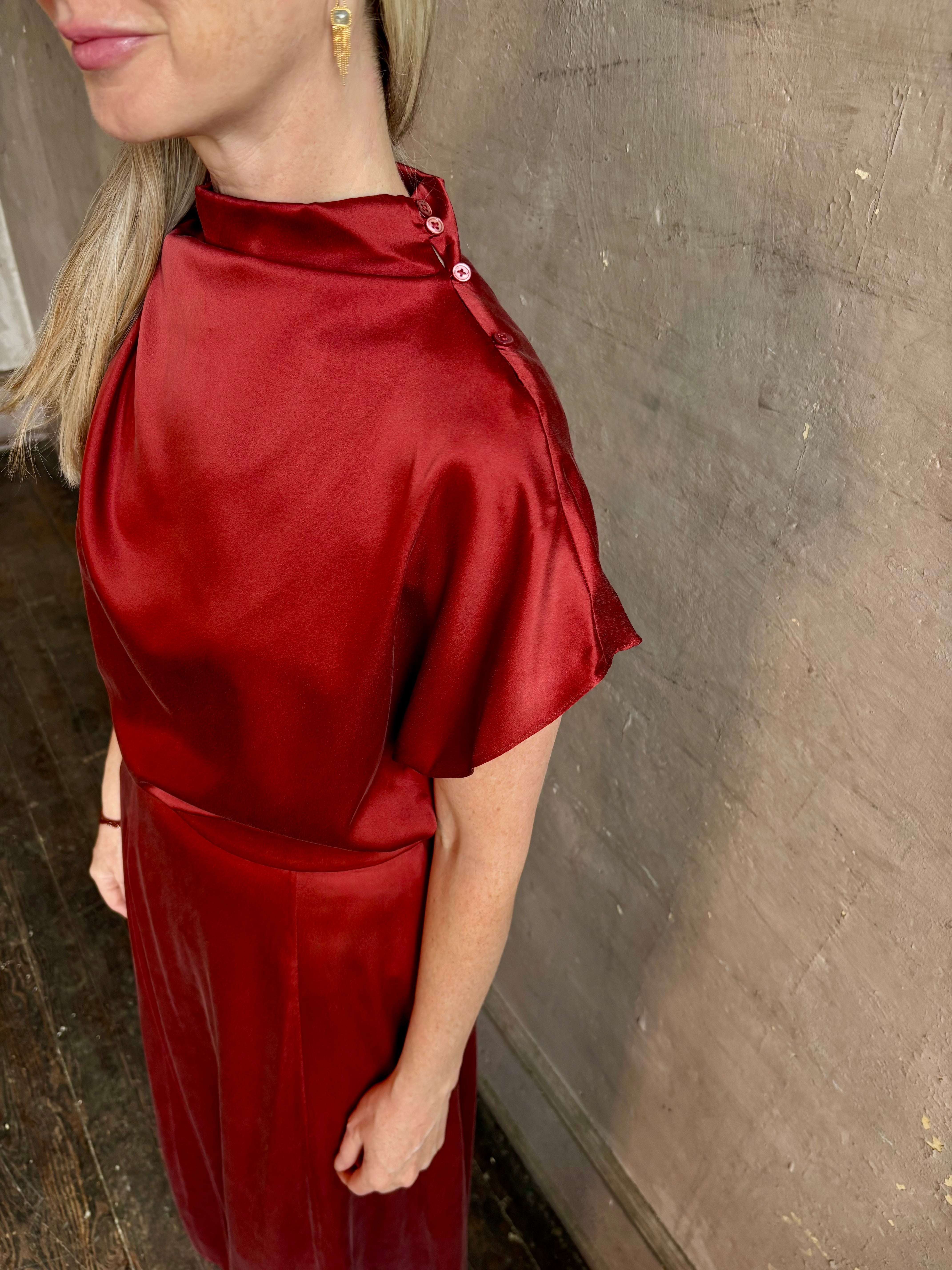 Mature woman wearing Wish You Would blouse from TWP rendered in a rich currant red and crafted from a luxurious silk blend with a mock neck,  asymetrical design and draping short sleeves shoulder button closure