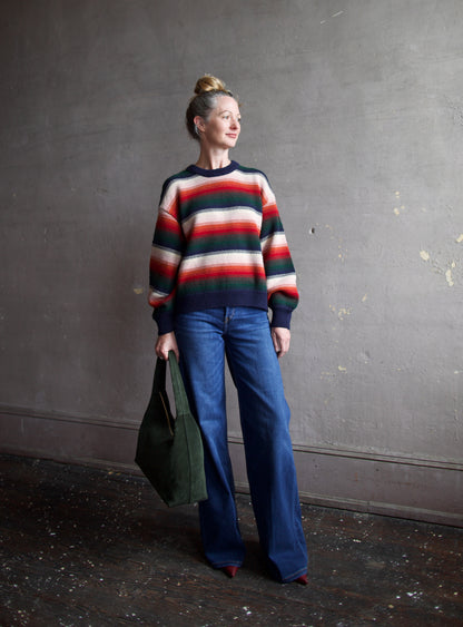 Image featuring a woman wearing the Bubble pullover sweater by The Great with a crew neckline, boxy fit, and drop shoulder in a navy, green, red, and cream stripe.