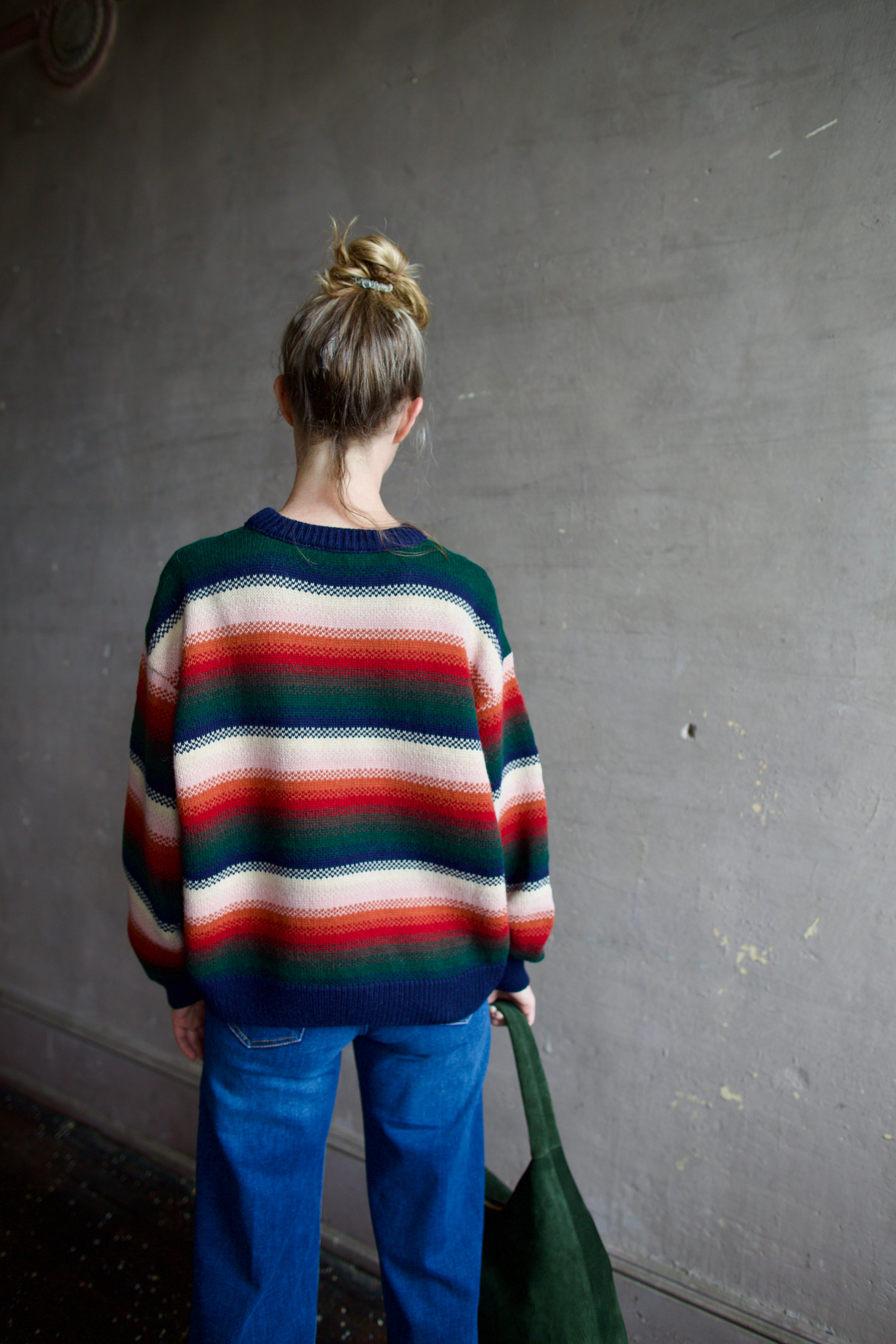 Image featuring a woman wearing the Bubble pullover sweater by The Great with a crew neckline, boxy fit, and drop shoulder in a navy, green, red, and cream stripe.