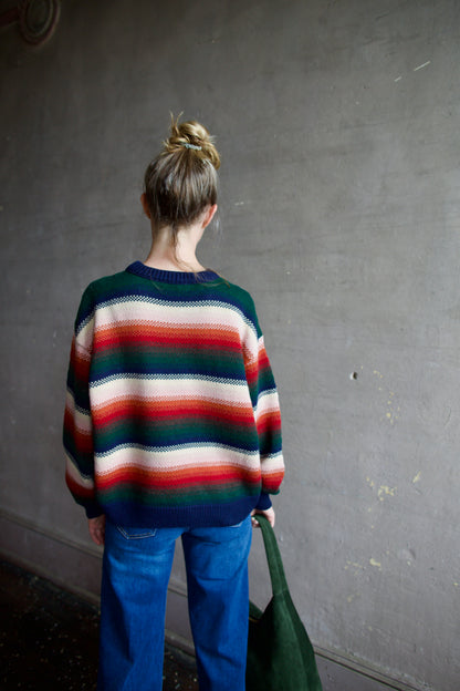 Image featuring a woman wearing the Bubble pullover sweater by The Great with a crew neckline, boxy fit, and drop shoulder in a navy, green, red, and cream stripe.