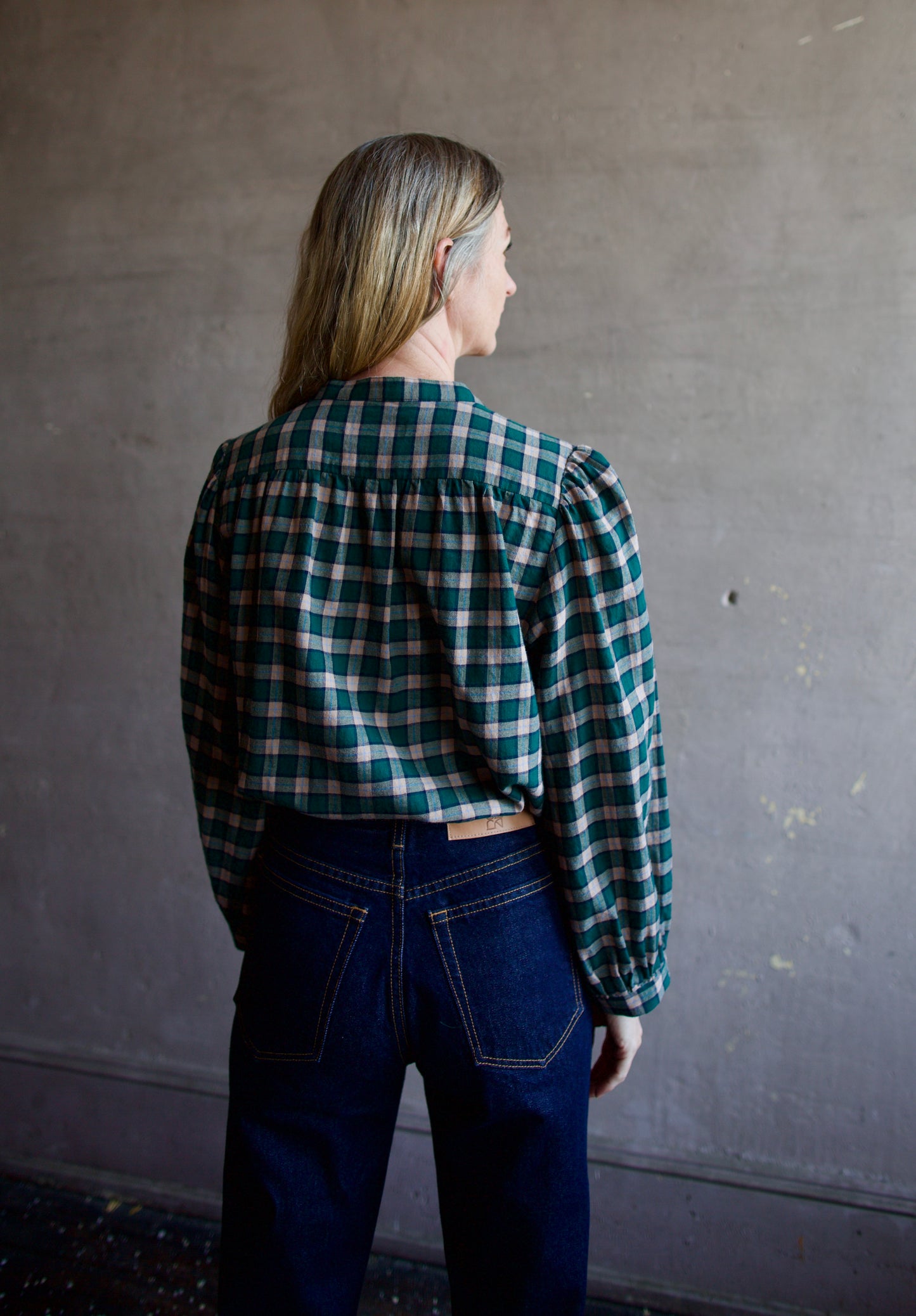 Image featuring a woman wearing the Clara blouse by Trovata features a button front and a slight puff sleeve in green and pink plaid.