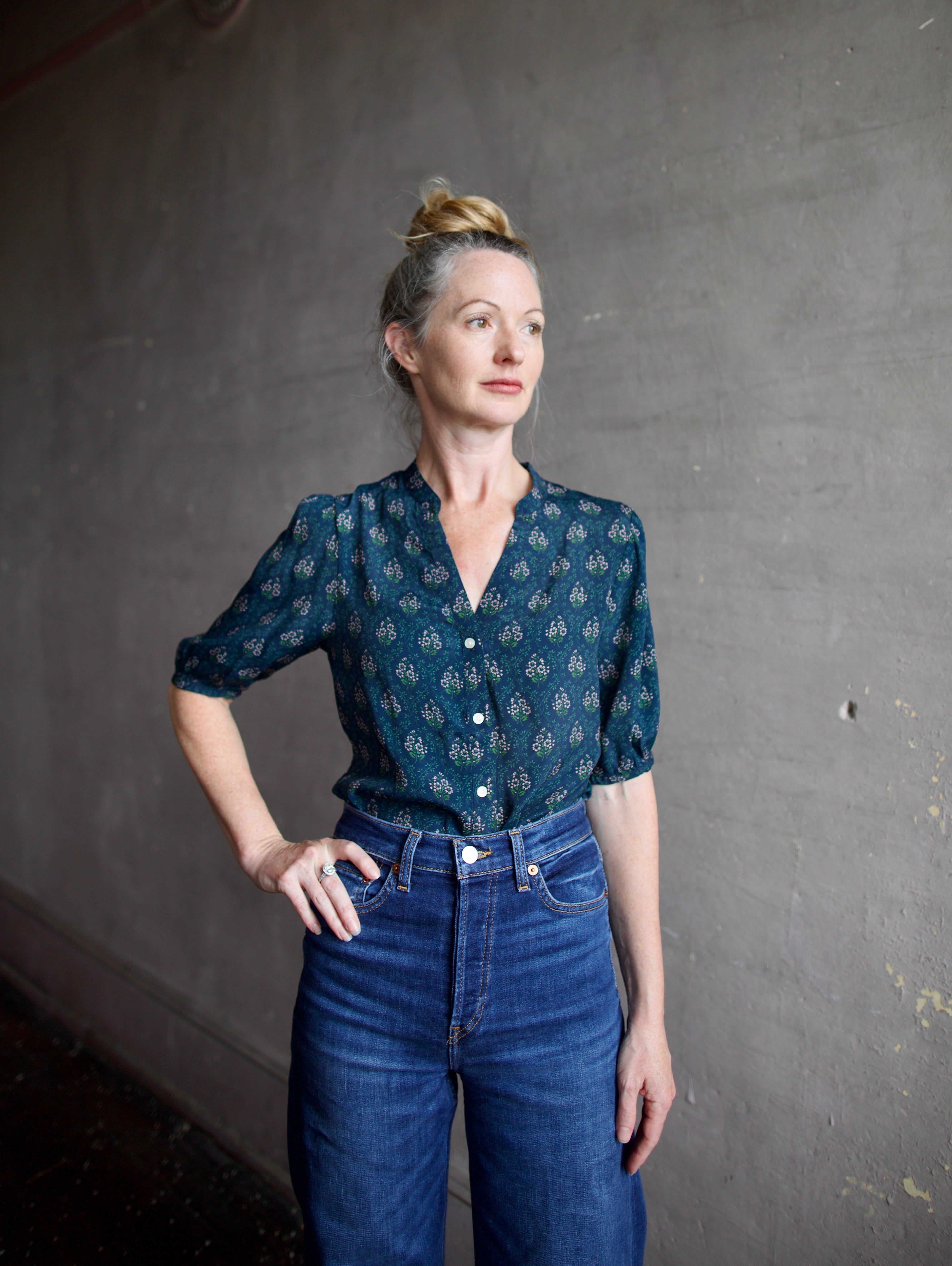 Image featuring a woman wearing the Dakota blouse by Trovata with a v-neck button front, elbow length sleeve in navy with pink and green flower blockprint.