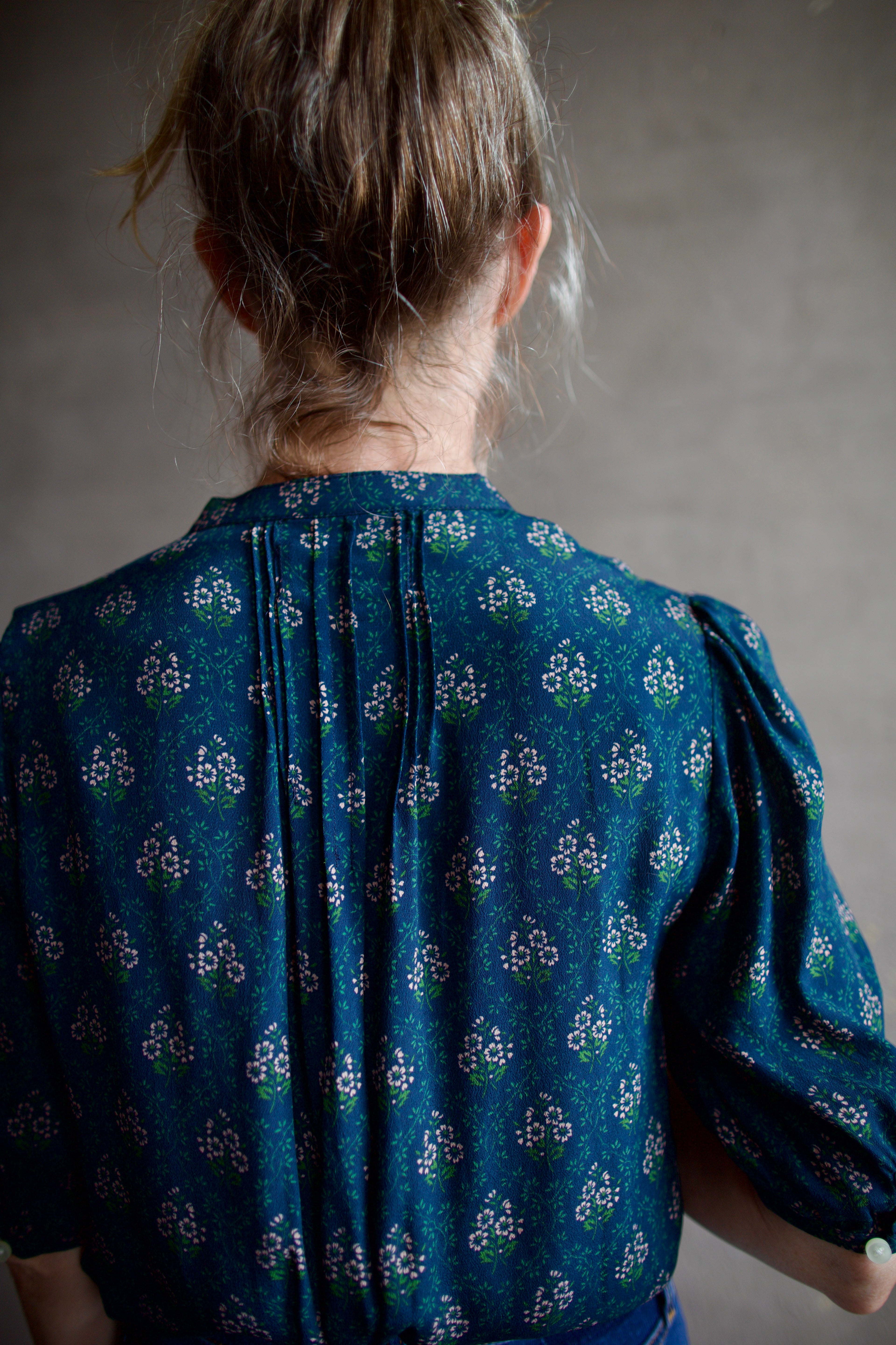 Image featuring a woman wearing the Dakota blouse by Trovata with a v-neck button front, elbow length sleeve in navy with pink and green flower blockprint.