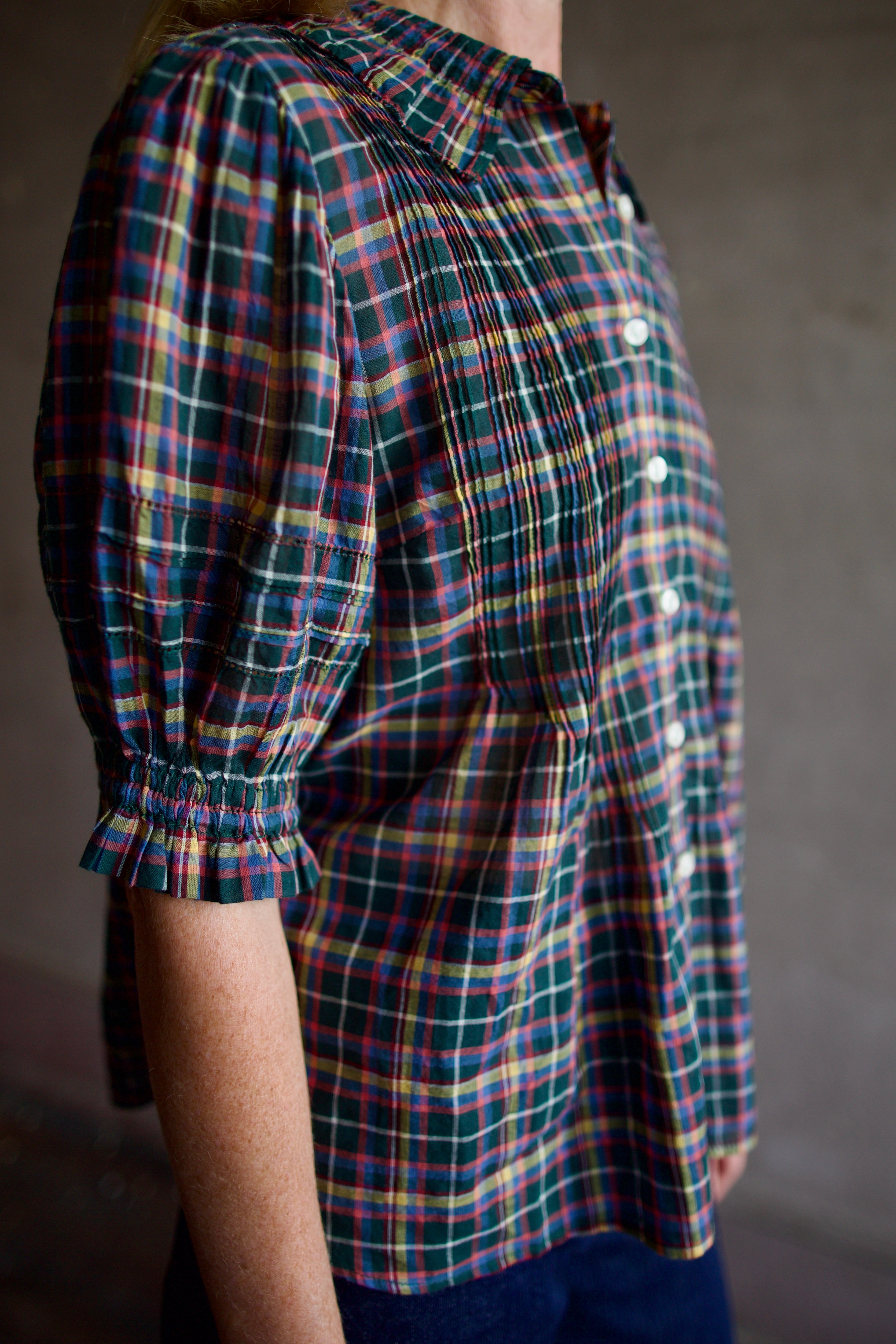 Model wearing Trovata Jess Blouse in cotton plaid with ruffle short sleeve detail pin tucking button front