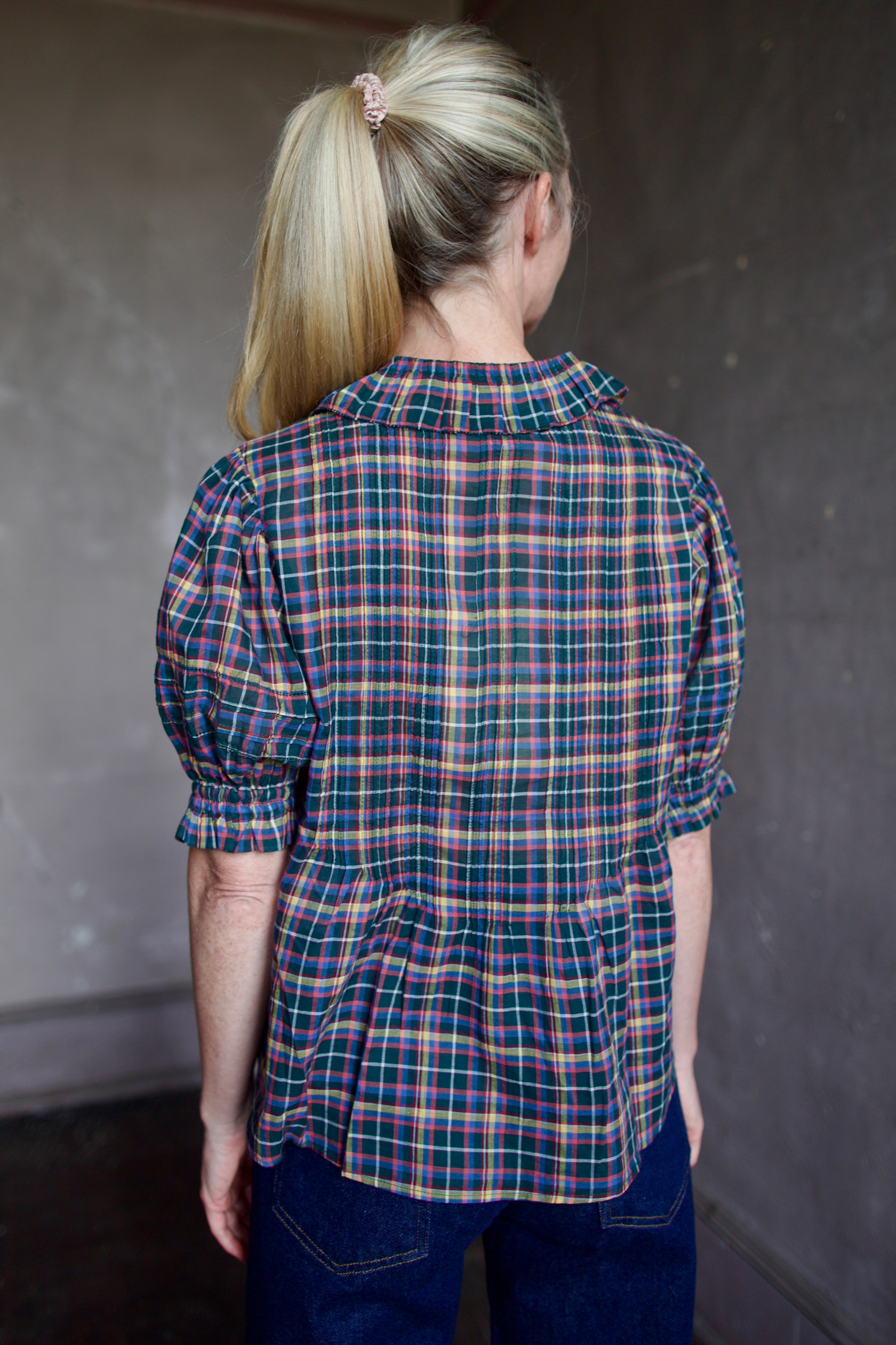 Model wearing Trovata Jess Blouse in cotton plaid with ruffle short sleeve detail pin tucking button front