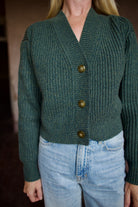 Mature woman wearing TWP Cropped Cardigan in Duffle Bag green ribbed cashmere V-neck long sleeves three button closure