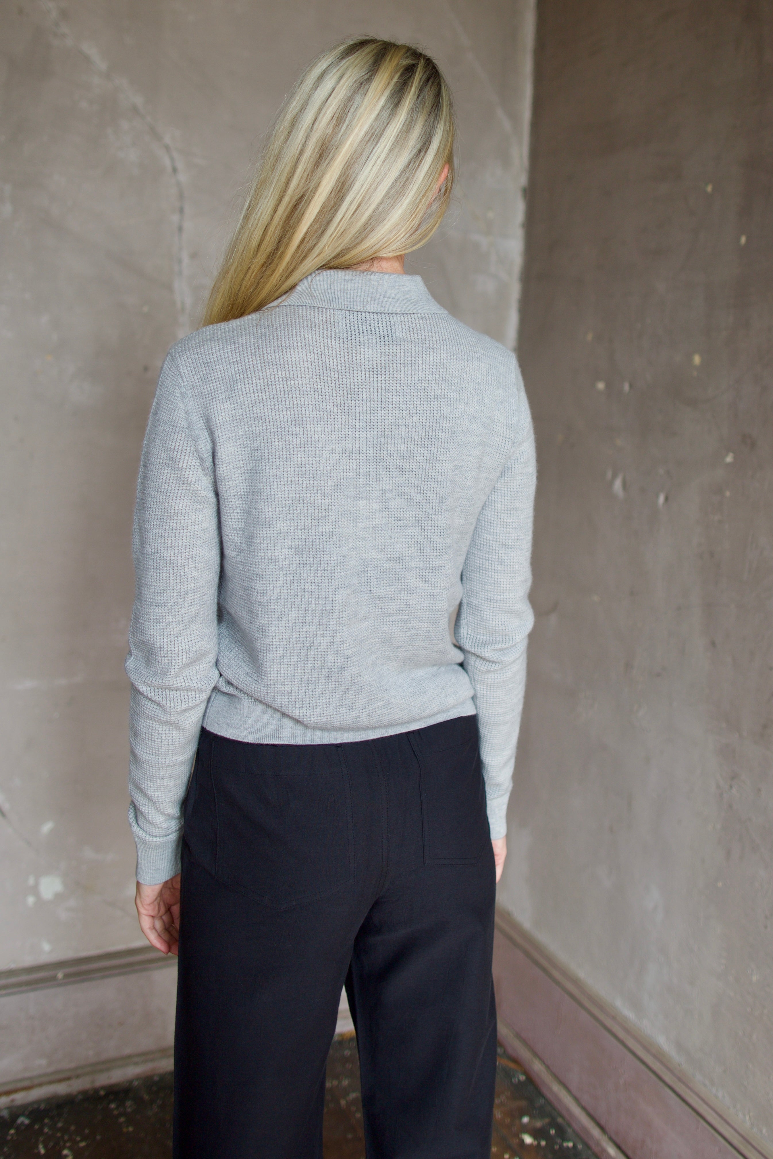 Model wearing TWP Jorden Polo in Light Heather Grey. Henley boasts premium cashmere construction for the ultimate elevated casual look.