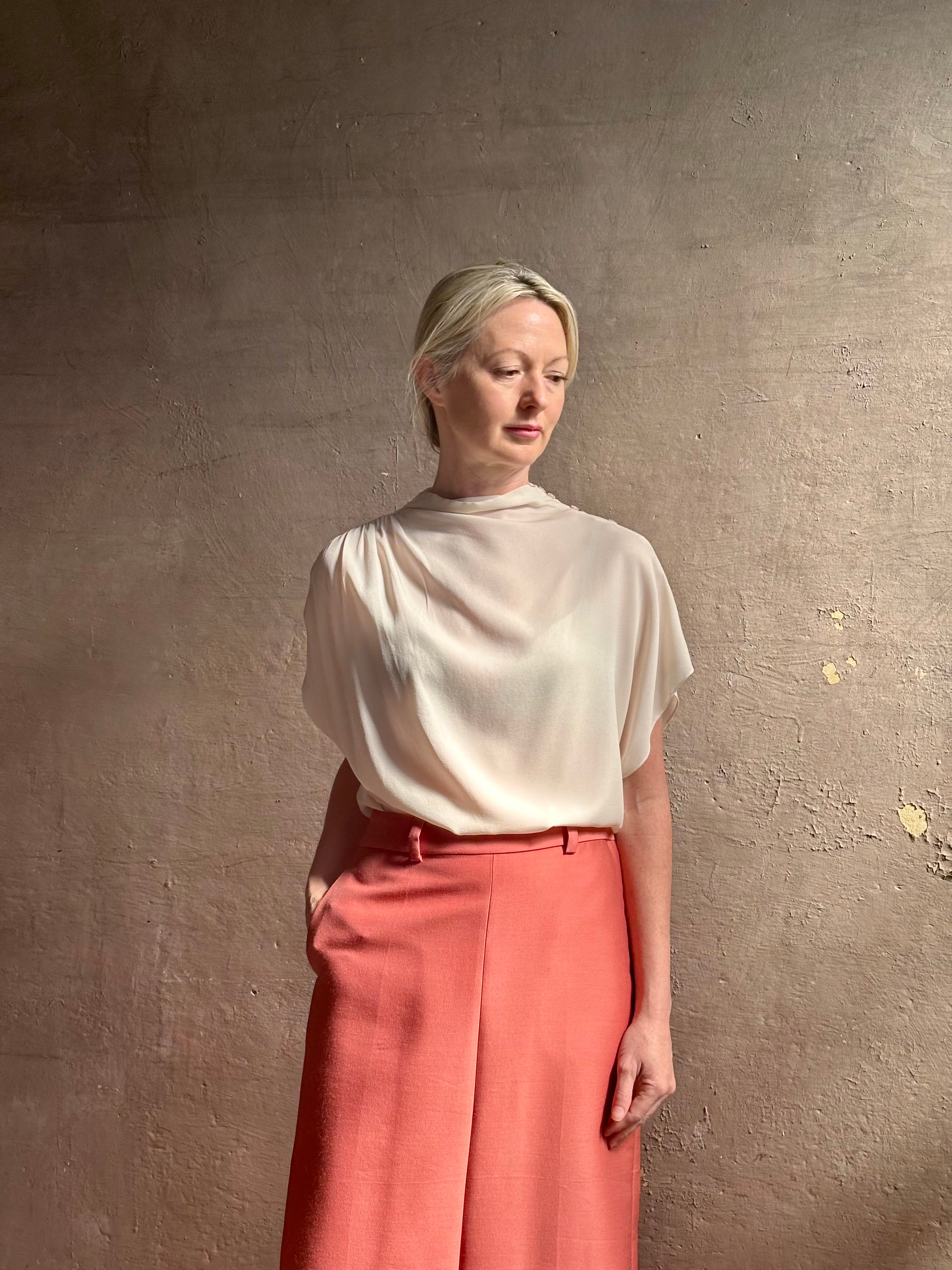 Mature woman wearing an elevated soft blush TWP silk blouse with beautifully draped short sleeves and modern asymmetrical design