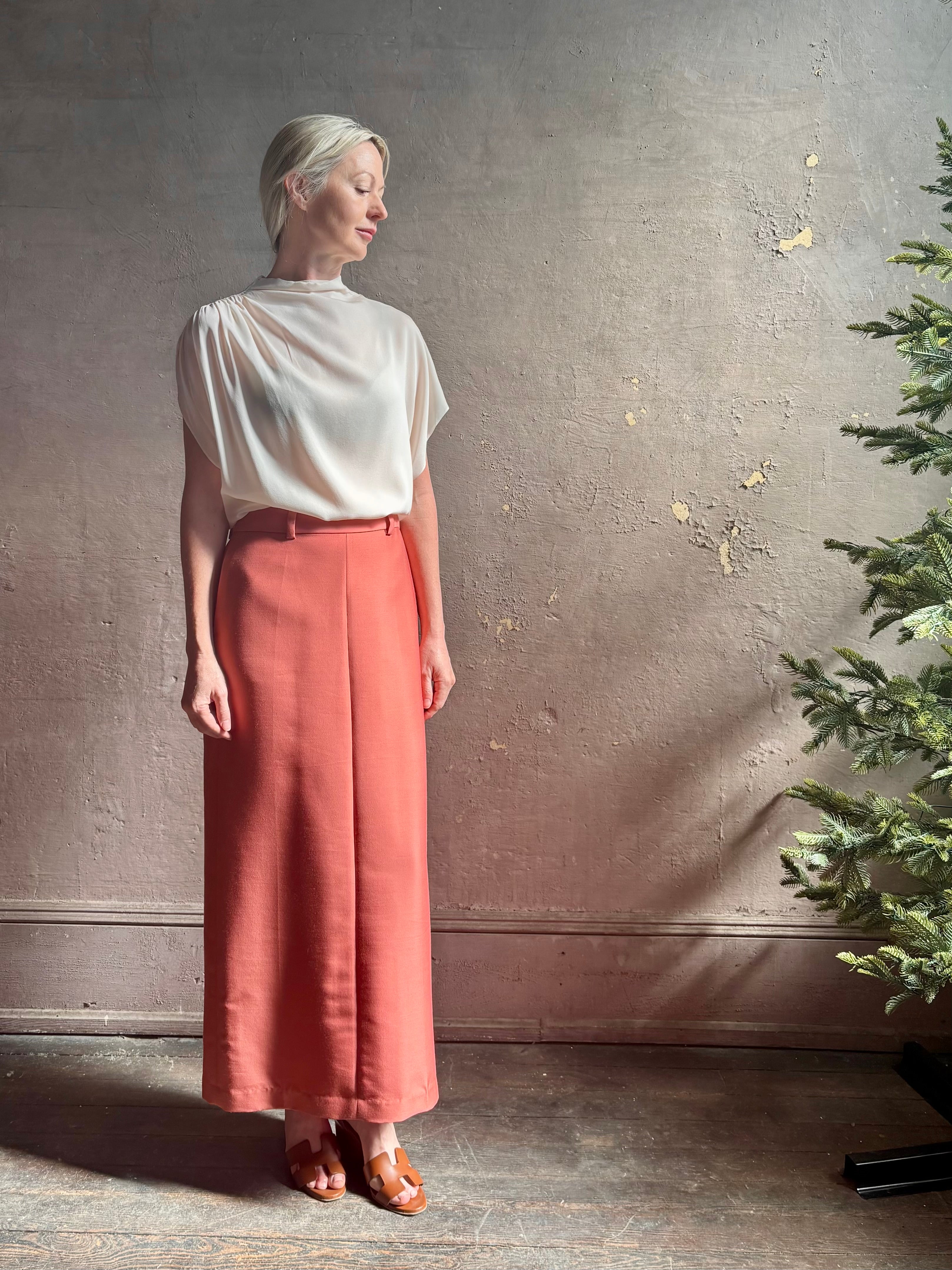 Mature woman wearing an elevated soft blush TWP silk blouse with beautifully draped short sleeves and modern asymmetrical design