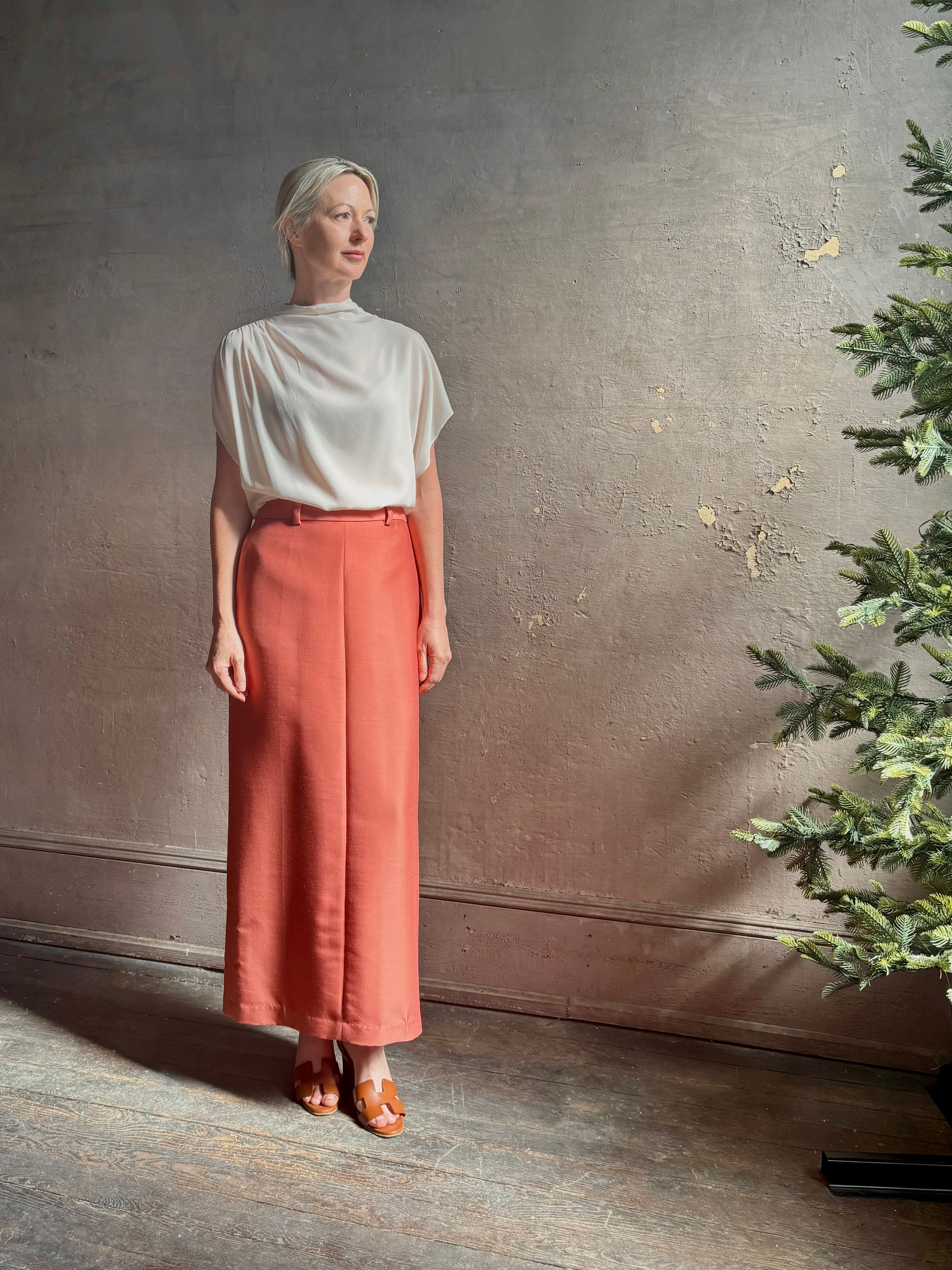 Mature woman wearing an elevated soft blush TWP silk blouse with beautifully draped short sleeves and modern asymmetrical design
