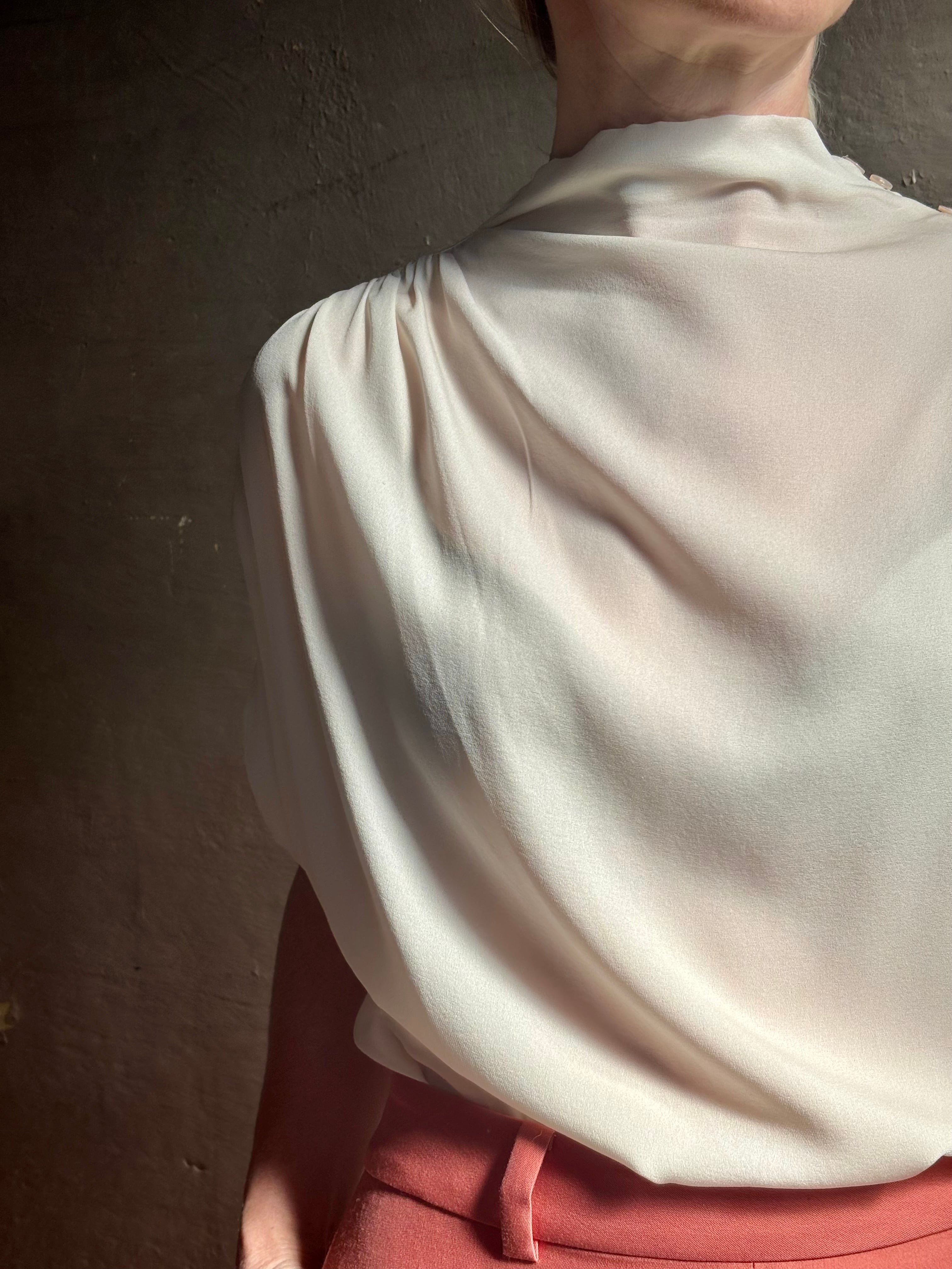 Mature woman wearing an elevated soft blush TWP silk blouse with beautifully draped short sleeves and modern asymmetrical design