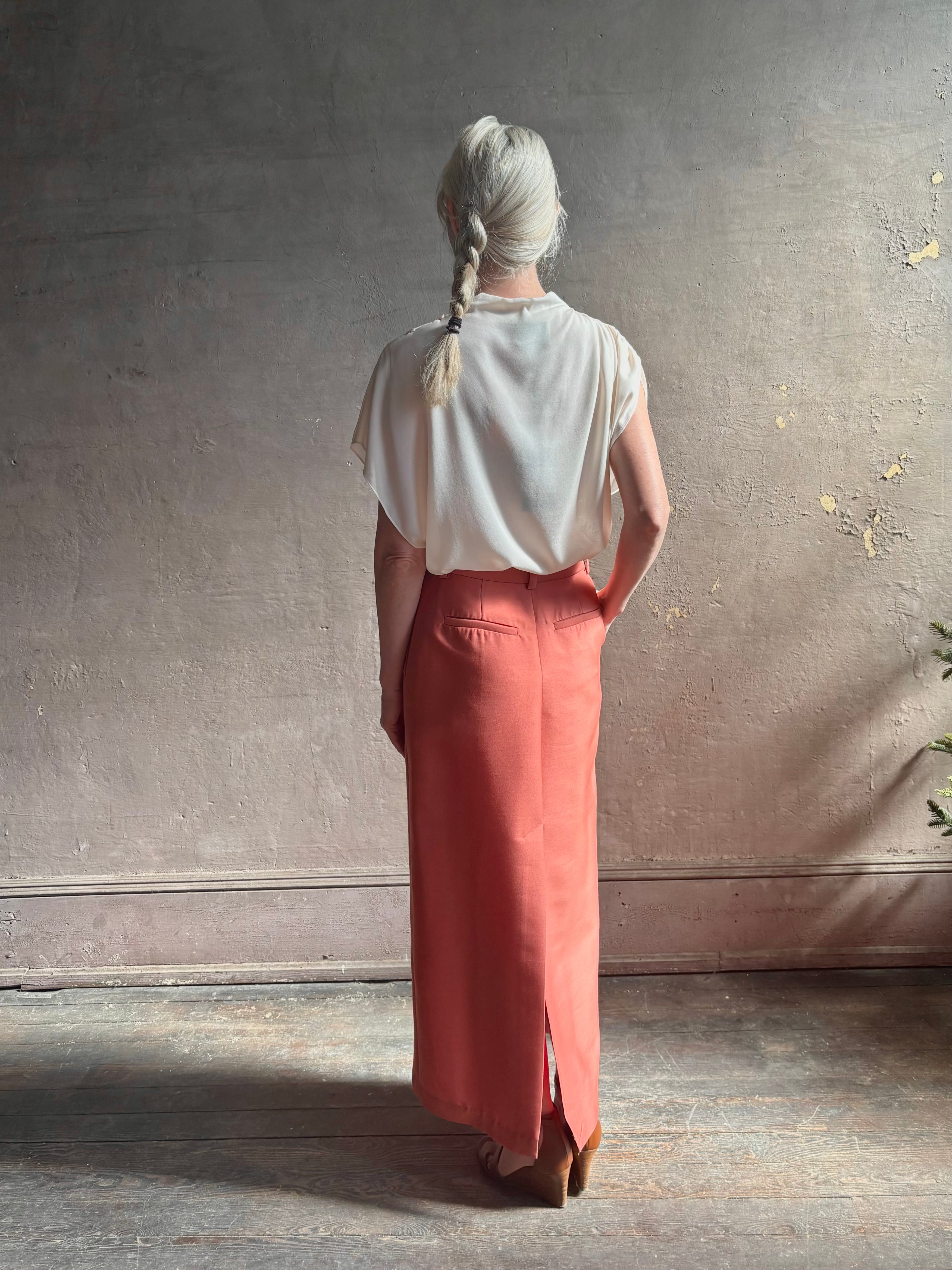 Mature woman wearing an elevated soft blush TWP silk blouse with beautifully draped short sleeves and modern asymmetrical design