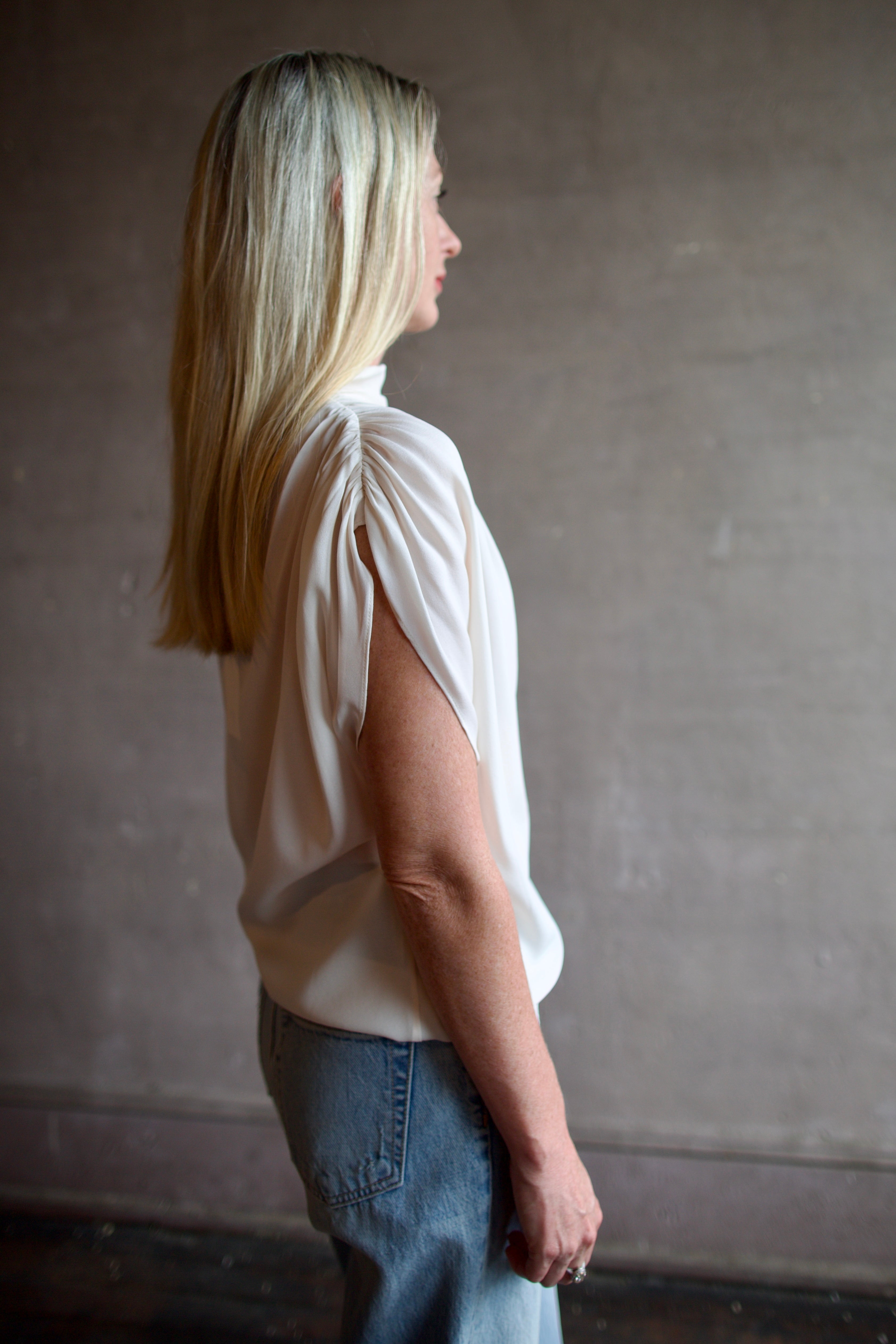 Mature model wearing a blush TWP silk blouse with ruffled sleeves and modern asymmetrical design