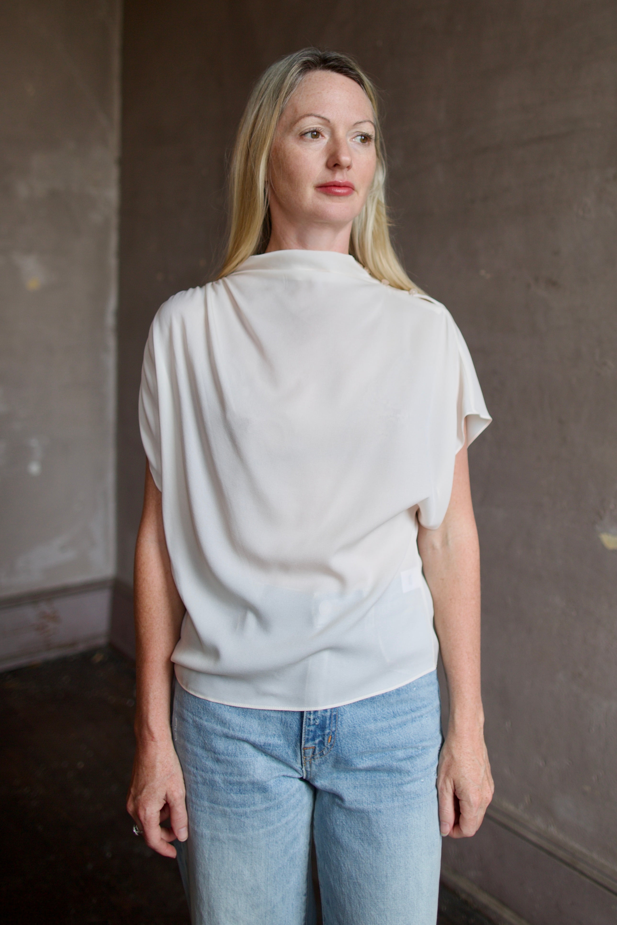 Mature model wearing a blush TWP silk blouse with ruffled sleeves and modern asymmetrical design
