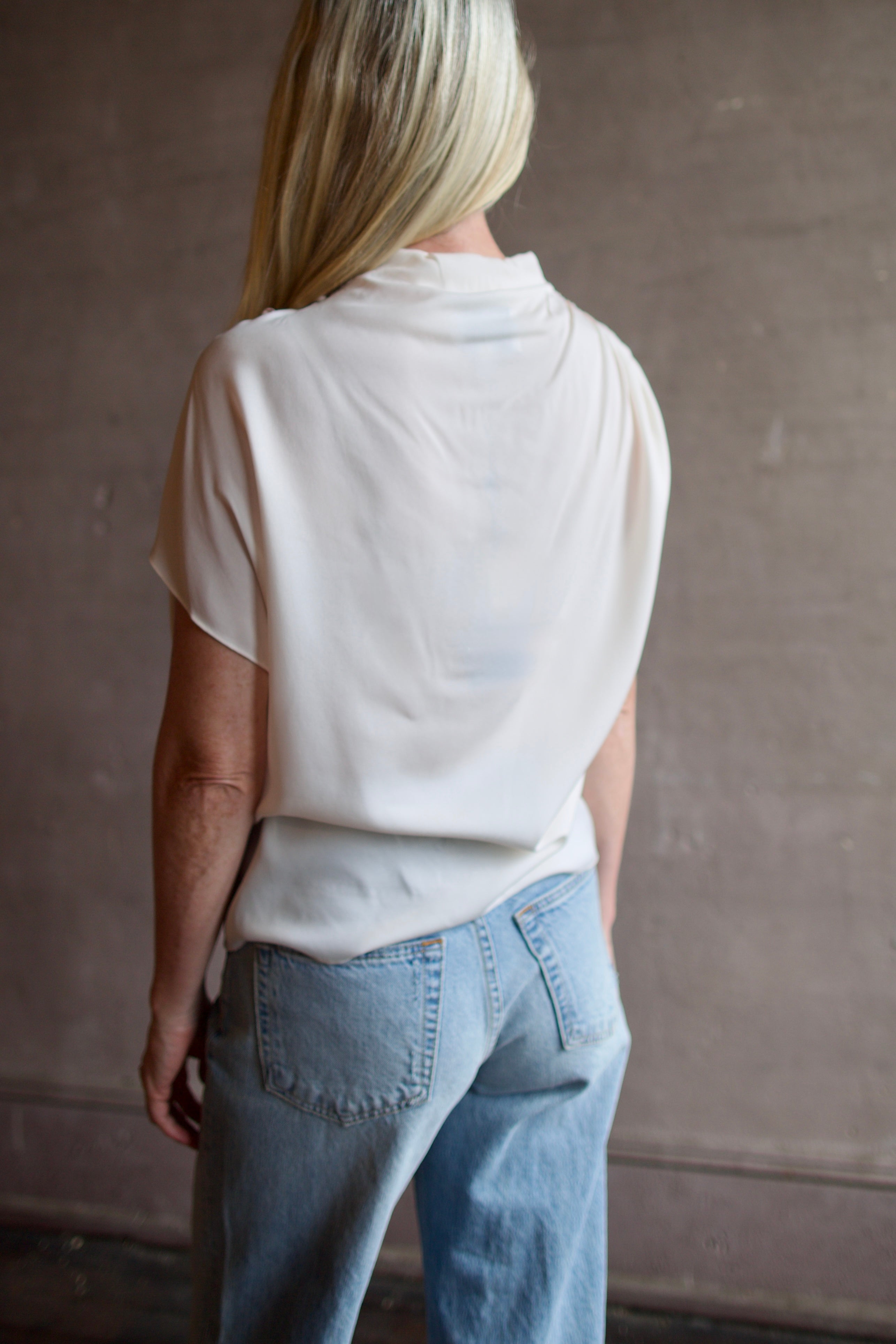 Mature model wearing a blush TWP silk blouse with ruffled sleeves and modern asymmetrical design