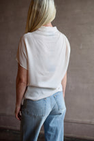 Mature model wearing a blush TWP silk blouse with ruffled sleeves and modern asymmetrical design