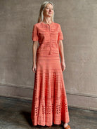 Woman wearing the feminine  Annisa Eyelet Knit A-line maxi skirt from Ulla Johnson rendered in a luminous coral hue and crafted from luxury knit with matching top
