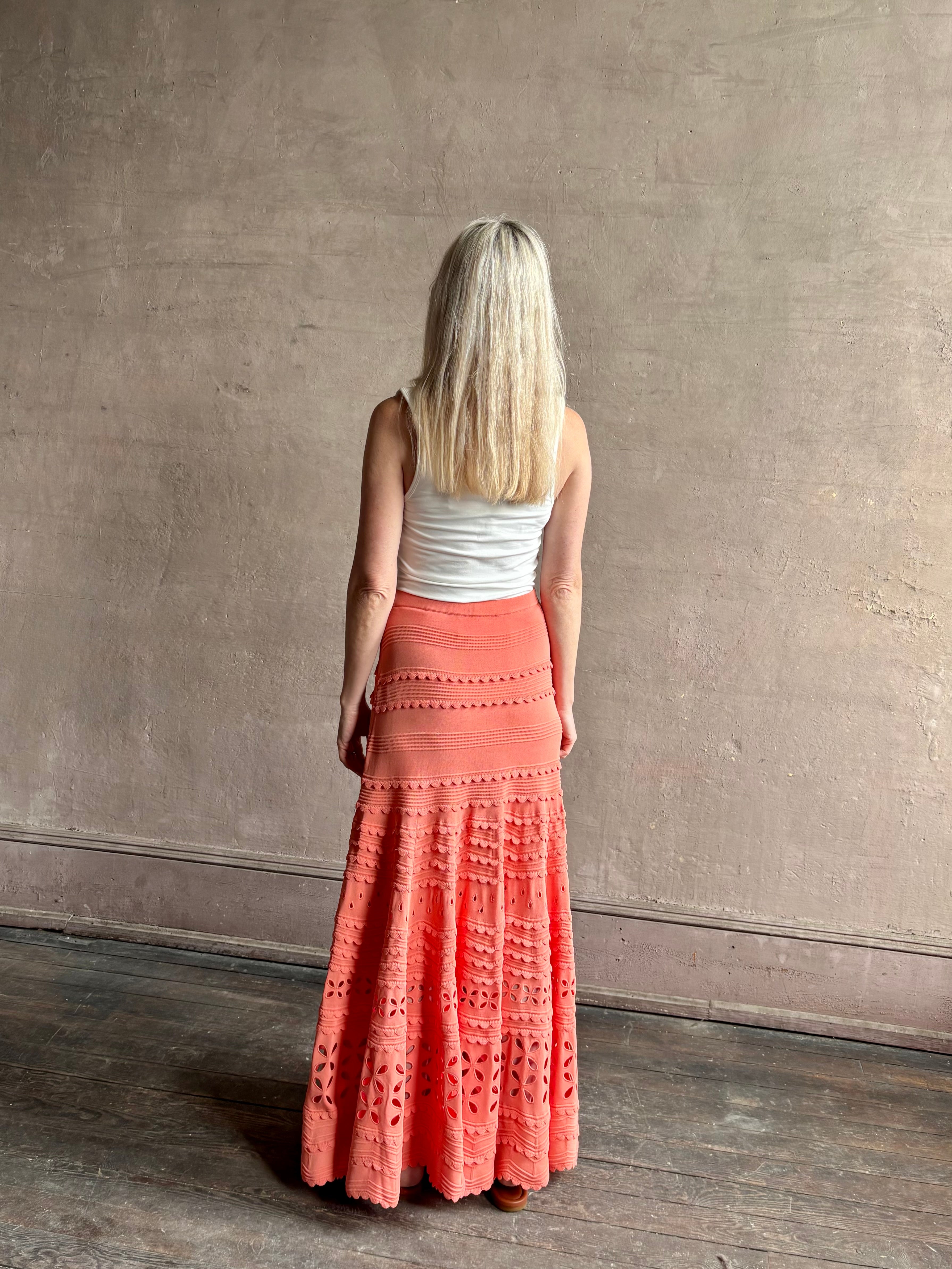 Woman wearing the feminine  Annisa Eyelet Knit A-line maxi skirt from Ulla Johnson rendered in a luminous coral hue and crafted from luxury knit 