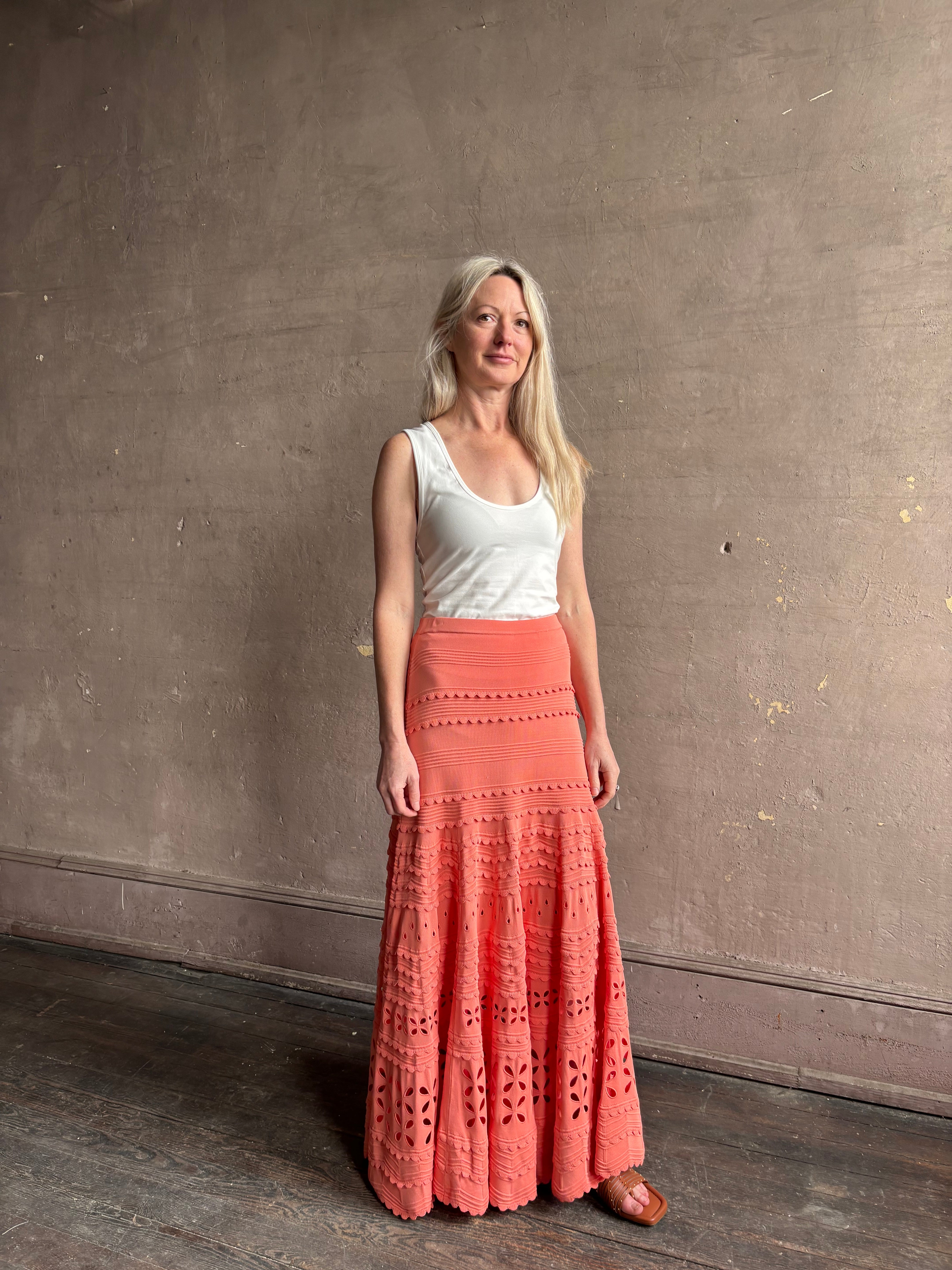 Woman wearing the feminine  Annisa Eyelet Knit A-line maxi skirt from Ulla Johnson rendered in a luminous coral hue and crafted from luxury knit 