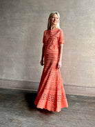 Woman wearing the feminine  Annisa Eyelet Knit A-line maxi skirt from Ulla Johnson rendered in a luminous coral hue and crafted from luxury knit with matching top