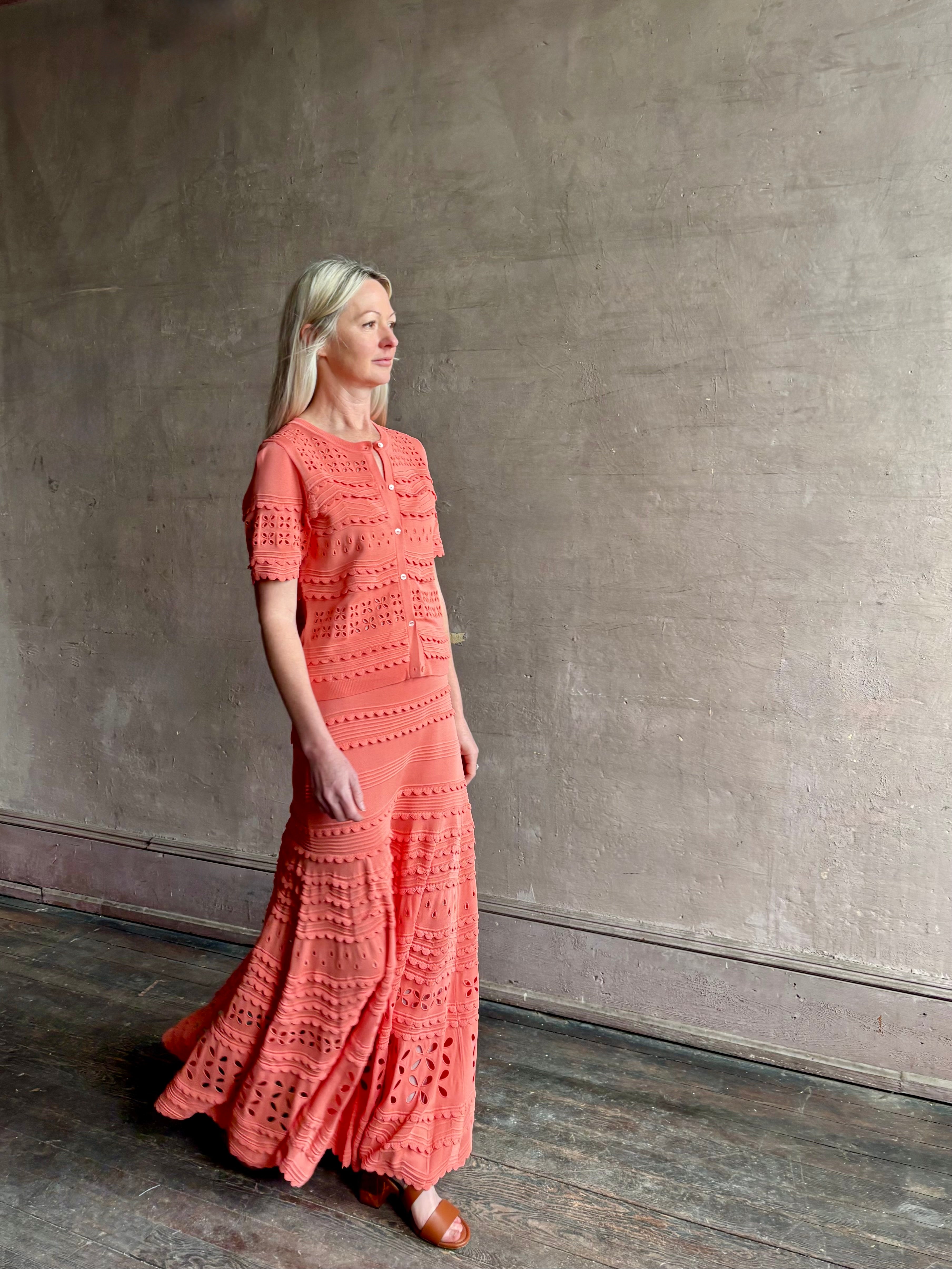 Woman wearing the feminine  Annisa Eyelet Knit A-line maxi skirt from Ulla Johnson rendered in a luminous coral hue and crafted from luxury knit with matching top