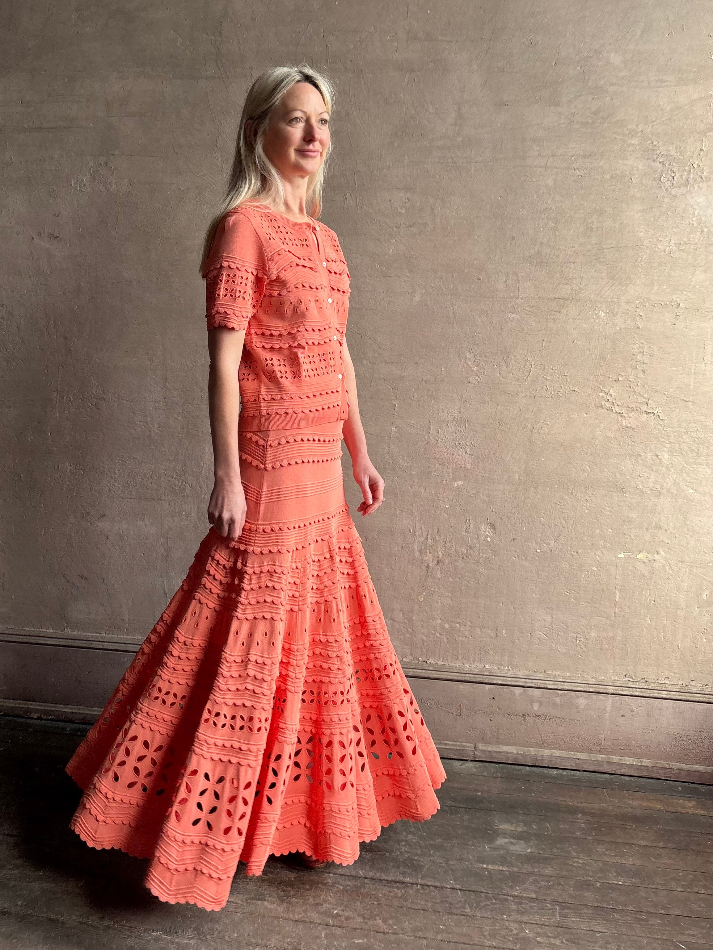 Woman wearing the feminine  Annisa Eyelet Knit A-line maxi skirt from Ulla Johnson rendered in a luminous coral hue and crafted from luxury knit with matching top
