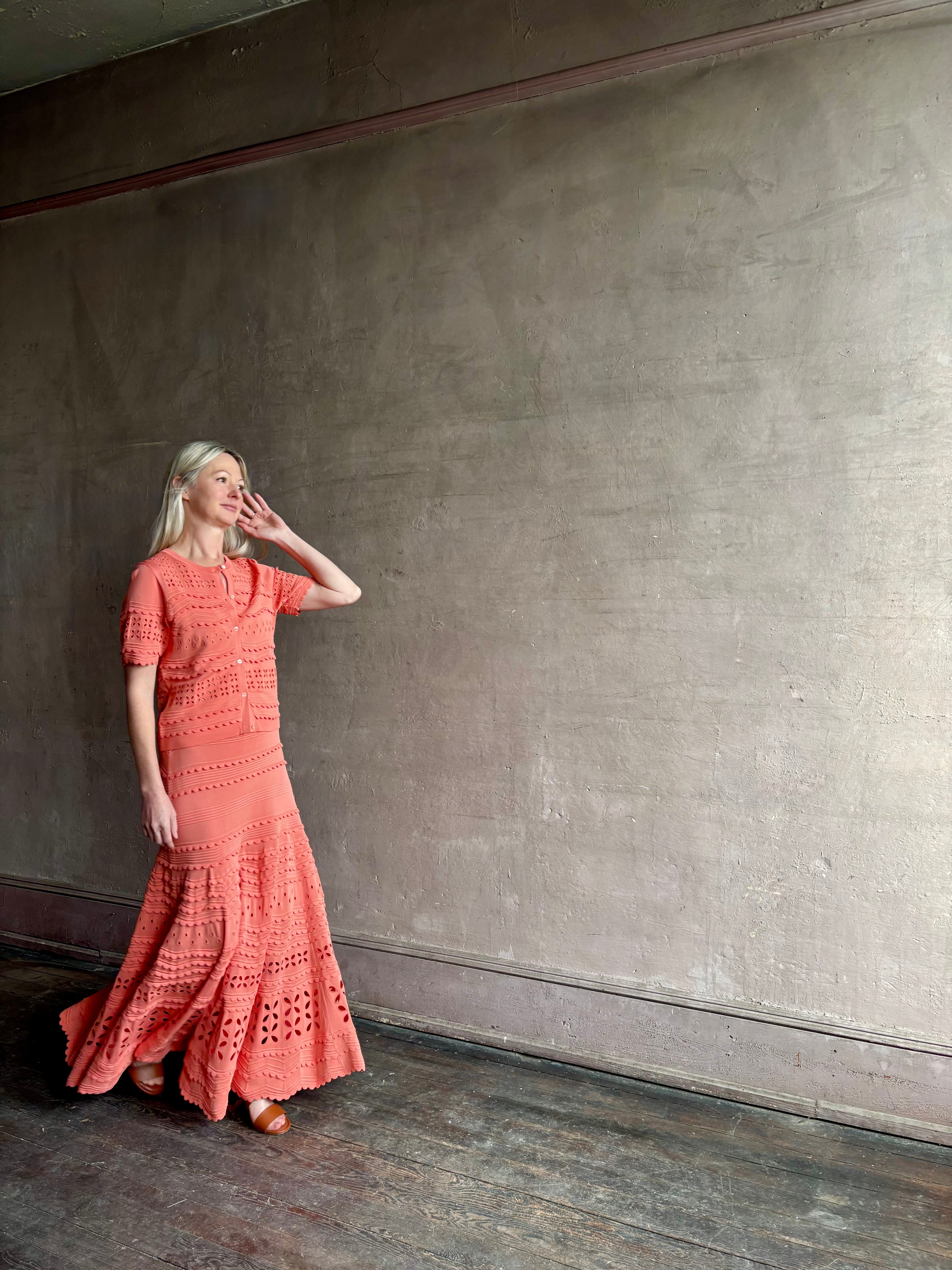 Woman wearing the feminine  Annisa Eyelet Knit A-line maxi skirt from Ulla Johnson rendered in a luminous coral hue and crafted from luxury knit with matching top