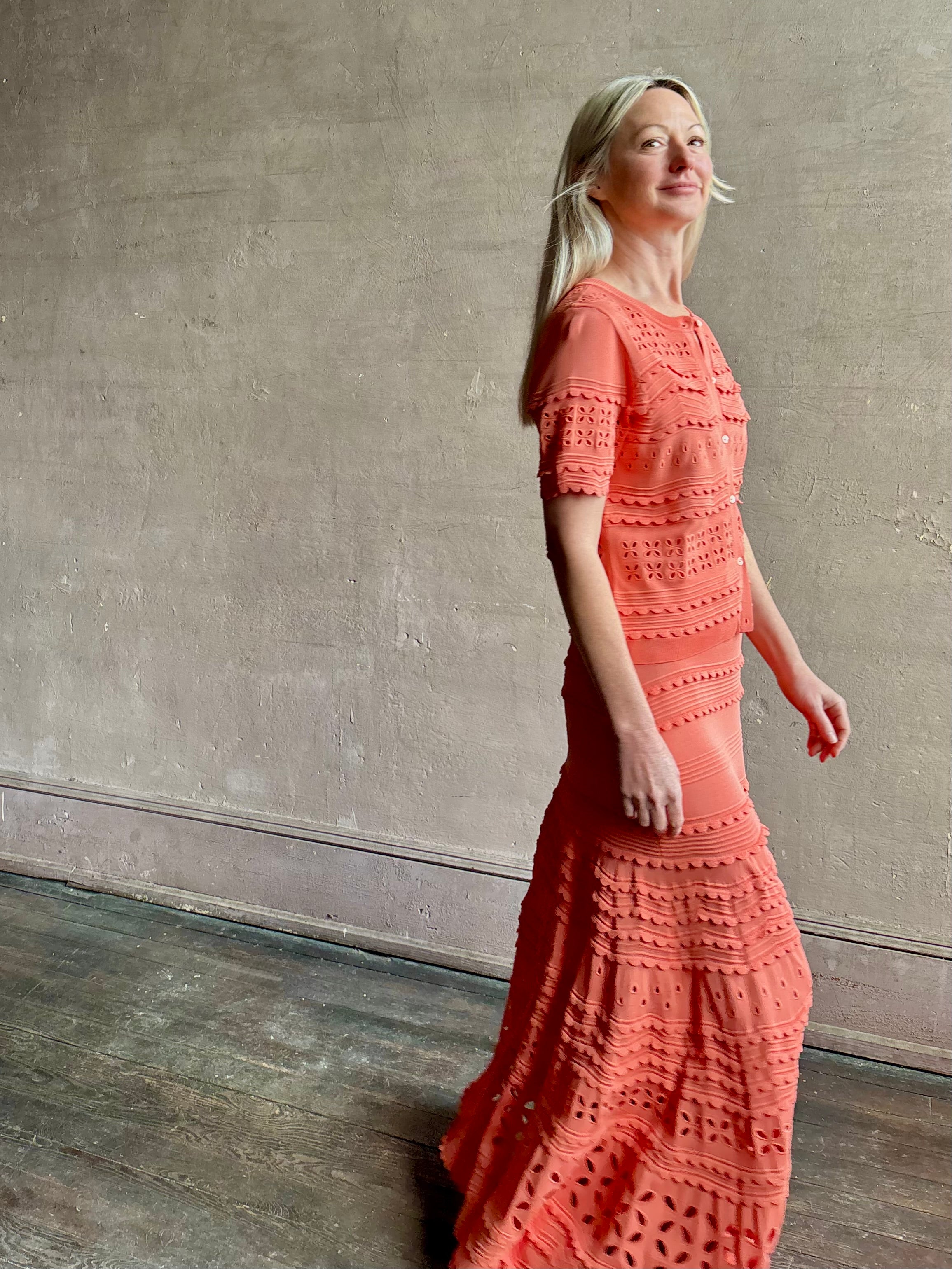 Woman wearing the feminine  Annisa Eyelet Knit A-line maxi skirt from Ulla Johnson rendered in a luminous coral hue and crafted from luxury knit with matching top