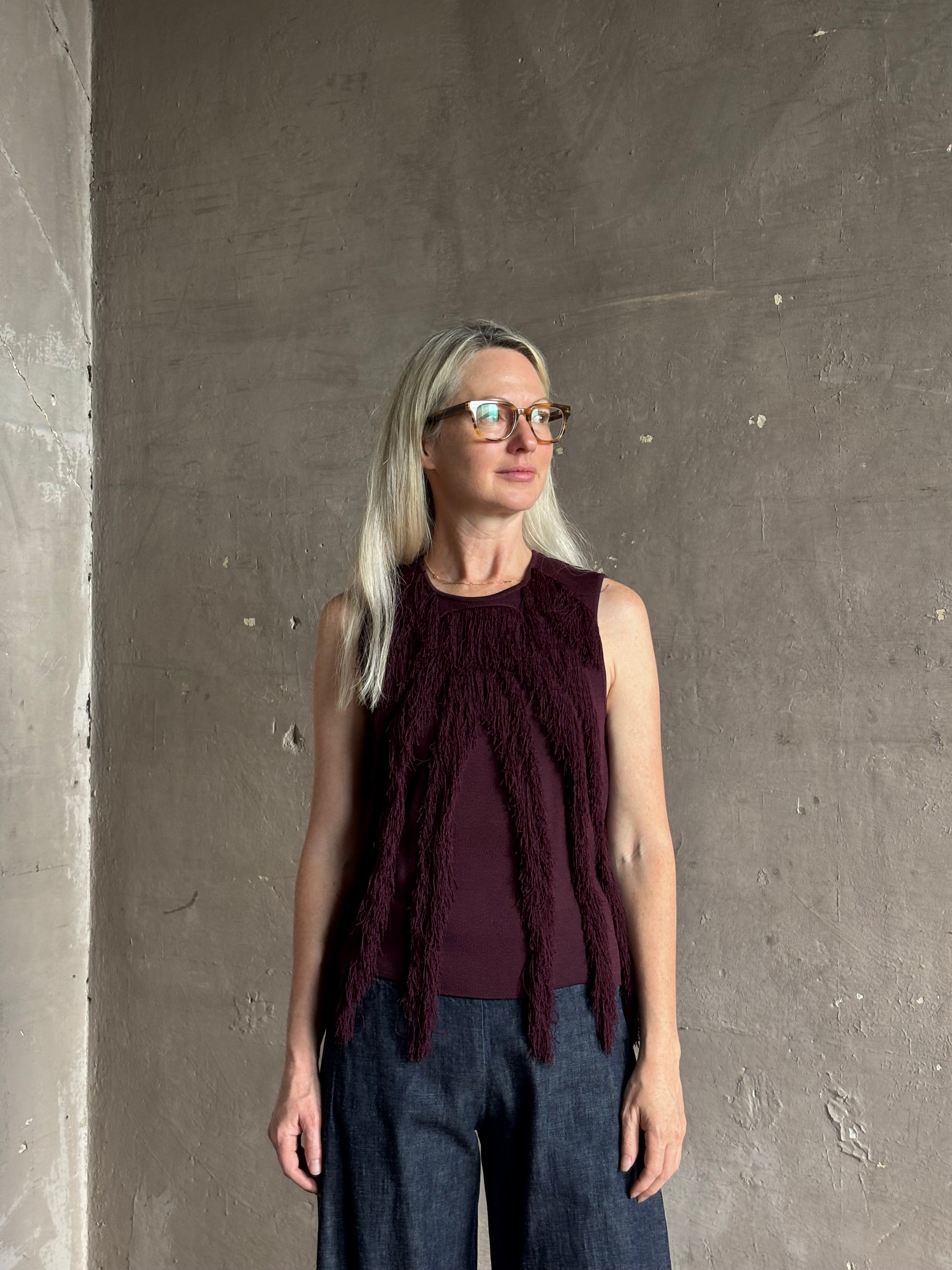Mature woman wearing sleeveless Ulla Johnson burgundy finge knit top with fun movement in an elevated viscose blend