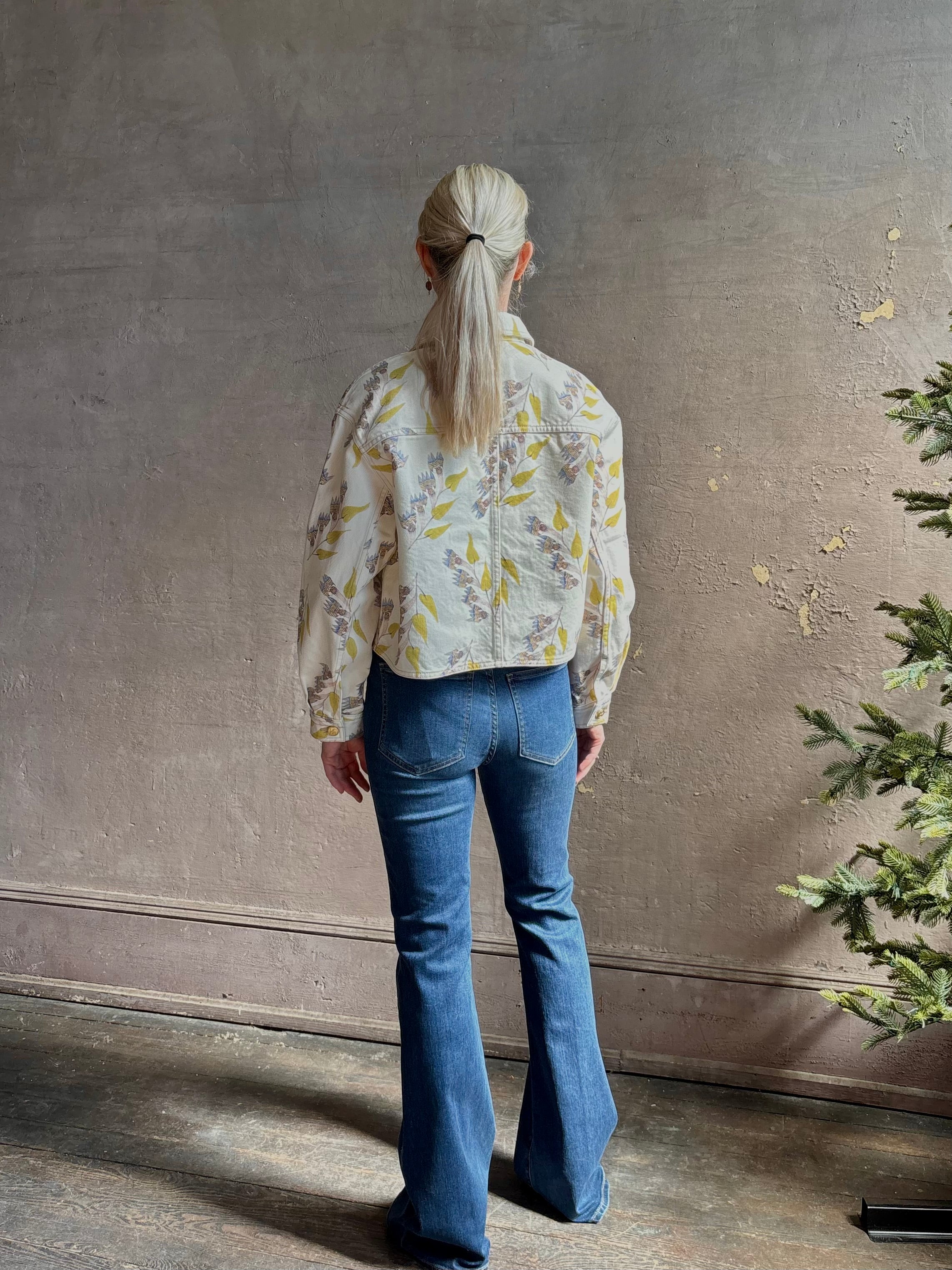 Mature woman wearing designer ULLA JOHNSON Bobbi cotton denim Jacket in an artisan collaboration print Infinite Flower with gold buttons, front pockets and crop length cool girl vibe