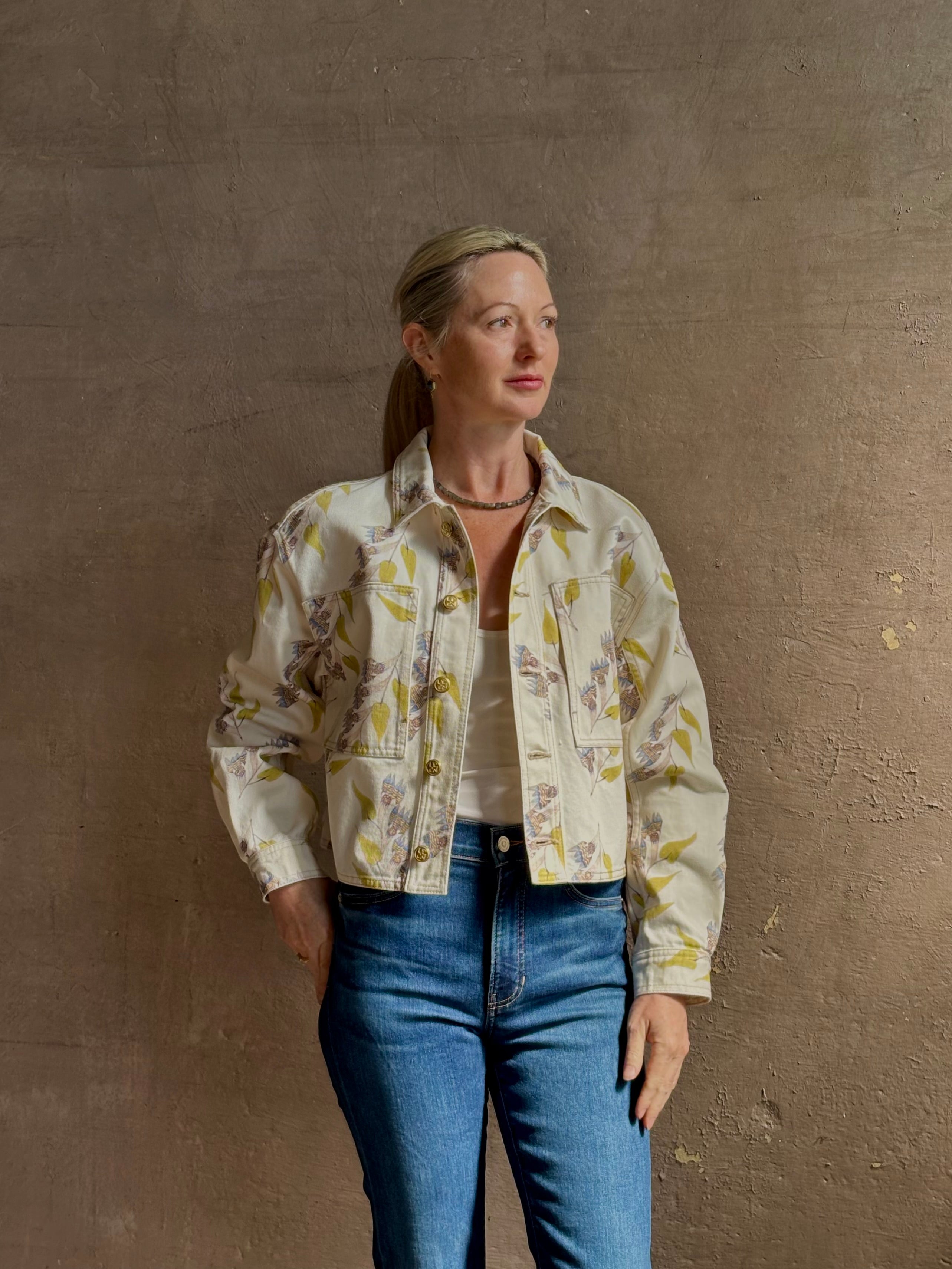 Mature woman wearing designer ULLA JOHNSON Bobbi cotton denim Jacket in an artisan collaboration print Infinite Flower with gold buttons, front pockets and crop length cool girl vibe