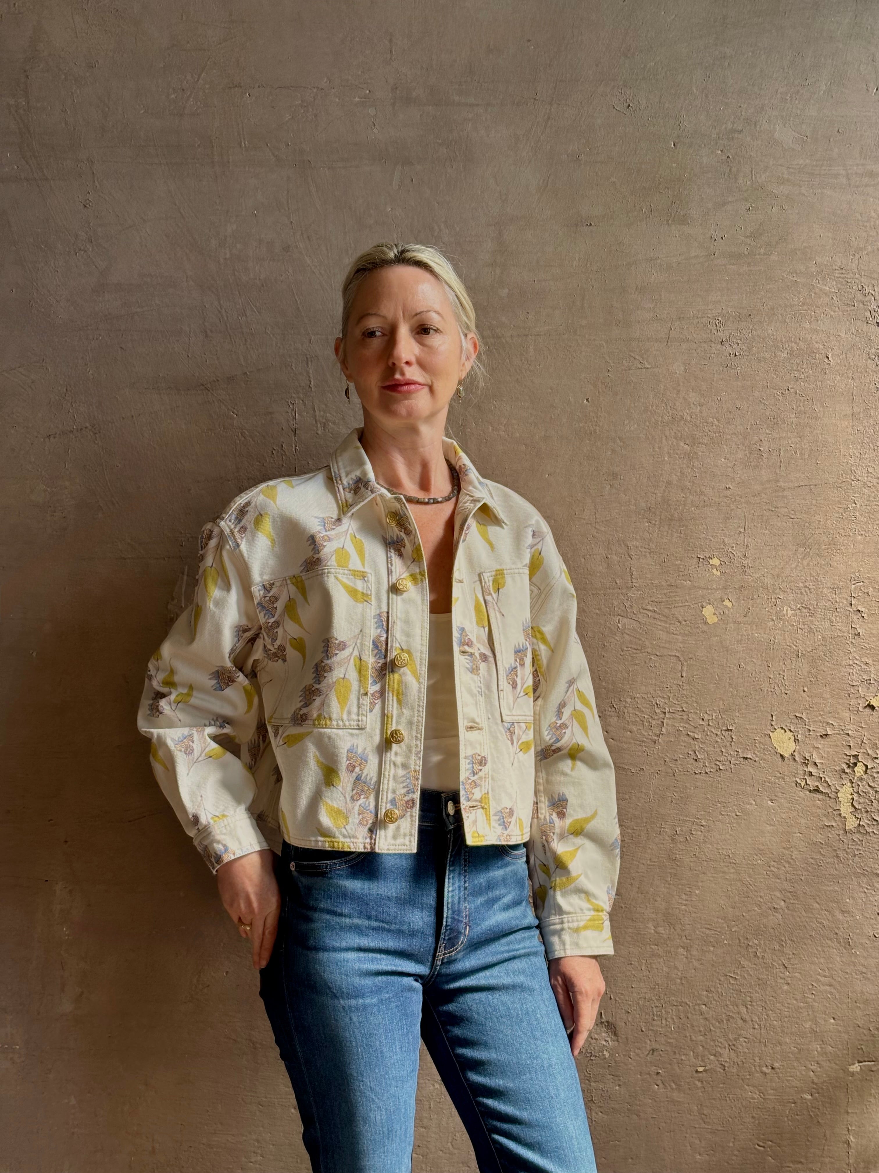 Mature woman wearing designer ULLA JOHNSON Bobbi cotton denim Jacket in an artisan collaboration print Infinite Flower with gold buttons, front pockets and crop length cool girl vibe