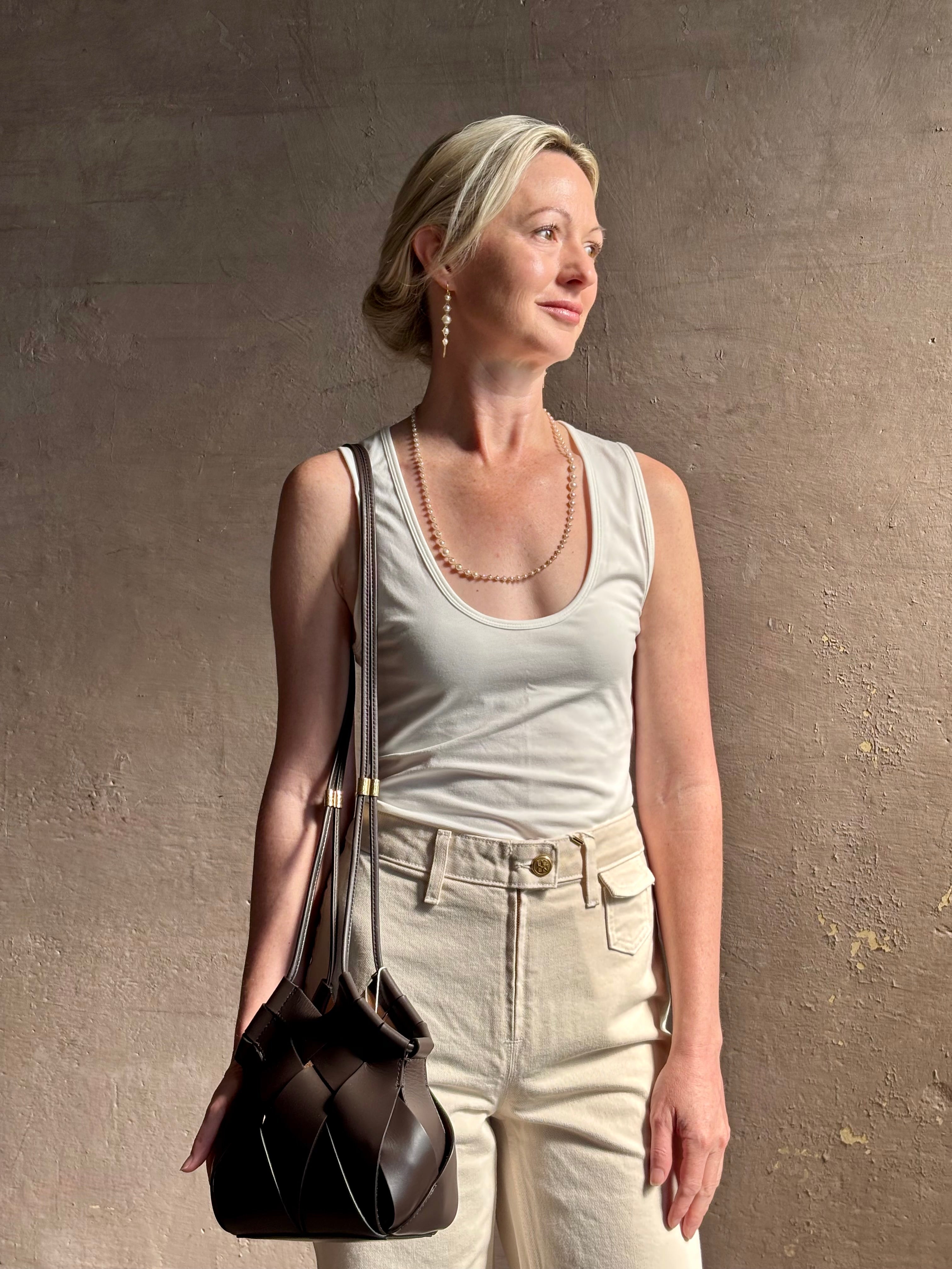 Mature woman with a Charlotte Crossbody from Ulla Johnson luxury woven Italian leather handbag rendered in a elegant neutral matte chocolate brown that easily coordinates with everything