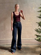 Mature woman wearing designer denim Colette Straight Leg Jean from Ulla Johnson offering American-made craftsmanship to a clean, timeless, and thoroughly modern everyday silhouette rendered in a sophisticated dark wash and crafted from 100% cotton with twisted buckle detail at waistband