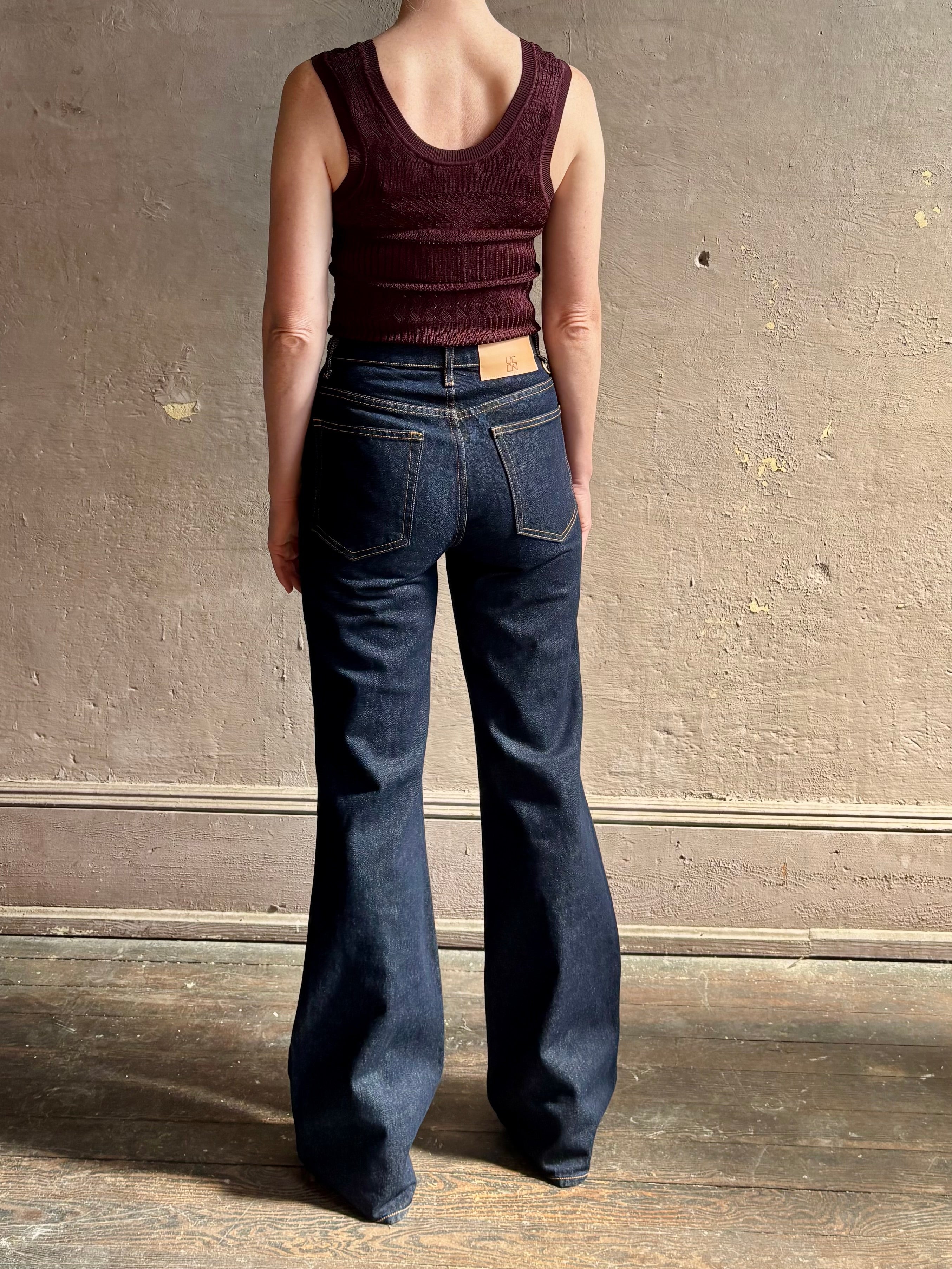 Mature woman wearing designer denim Colette Straight Leg Jean from Ulla Johnson offering American-made craftsmanship to a clean, timeless, and thoroughly modern everyday silhouette rendered in a sophisticated dark wash and crafted from 100% cotton with twisted buckle detail at waistband